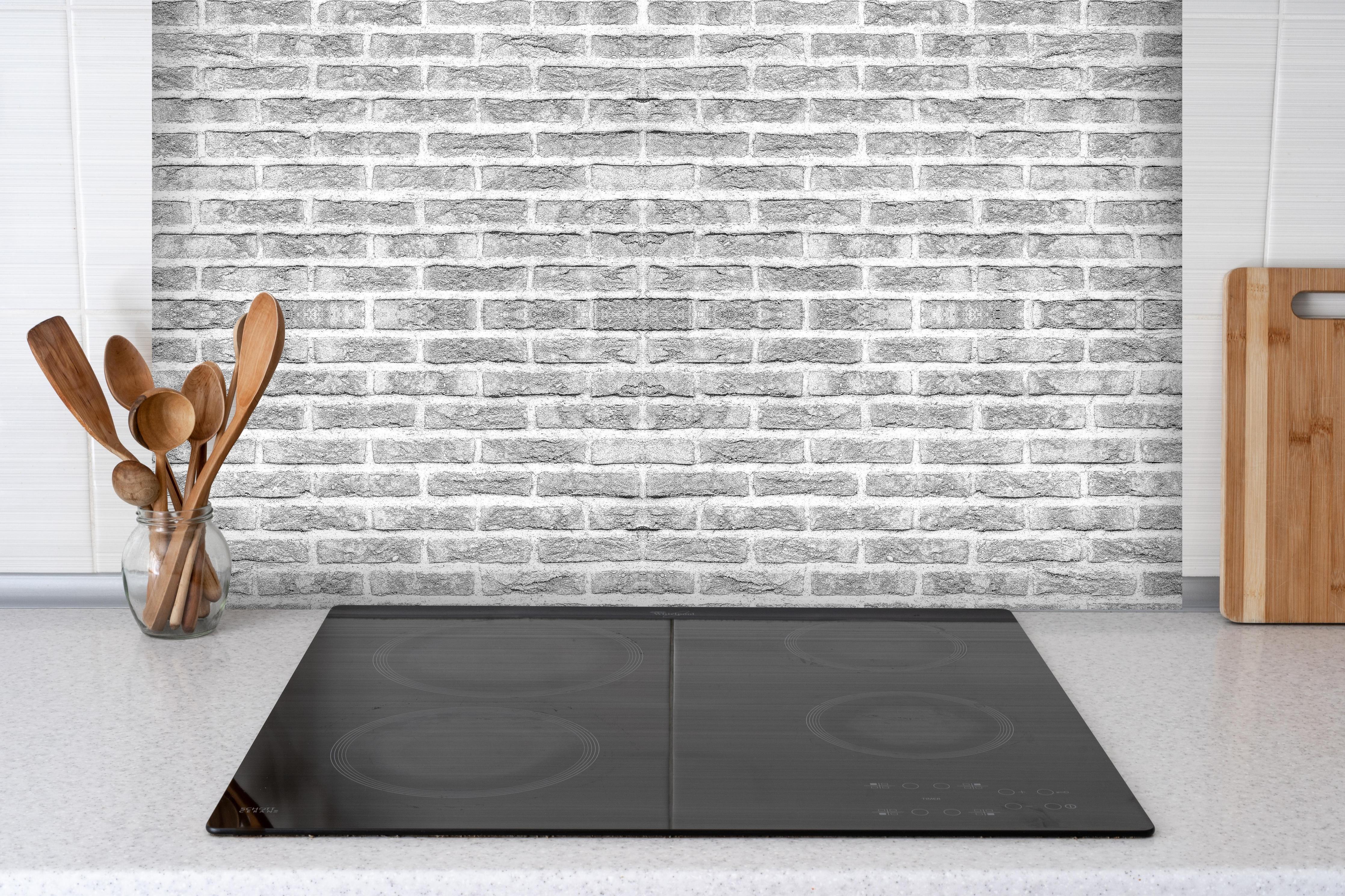 Spritzschutz - Graue alte Ziegelwand hinter einem Cerankochfeld zwischen Holz-Kochutensilien