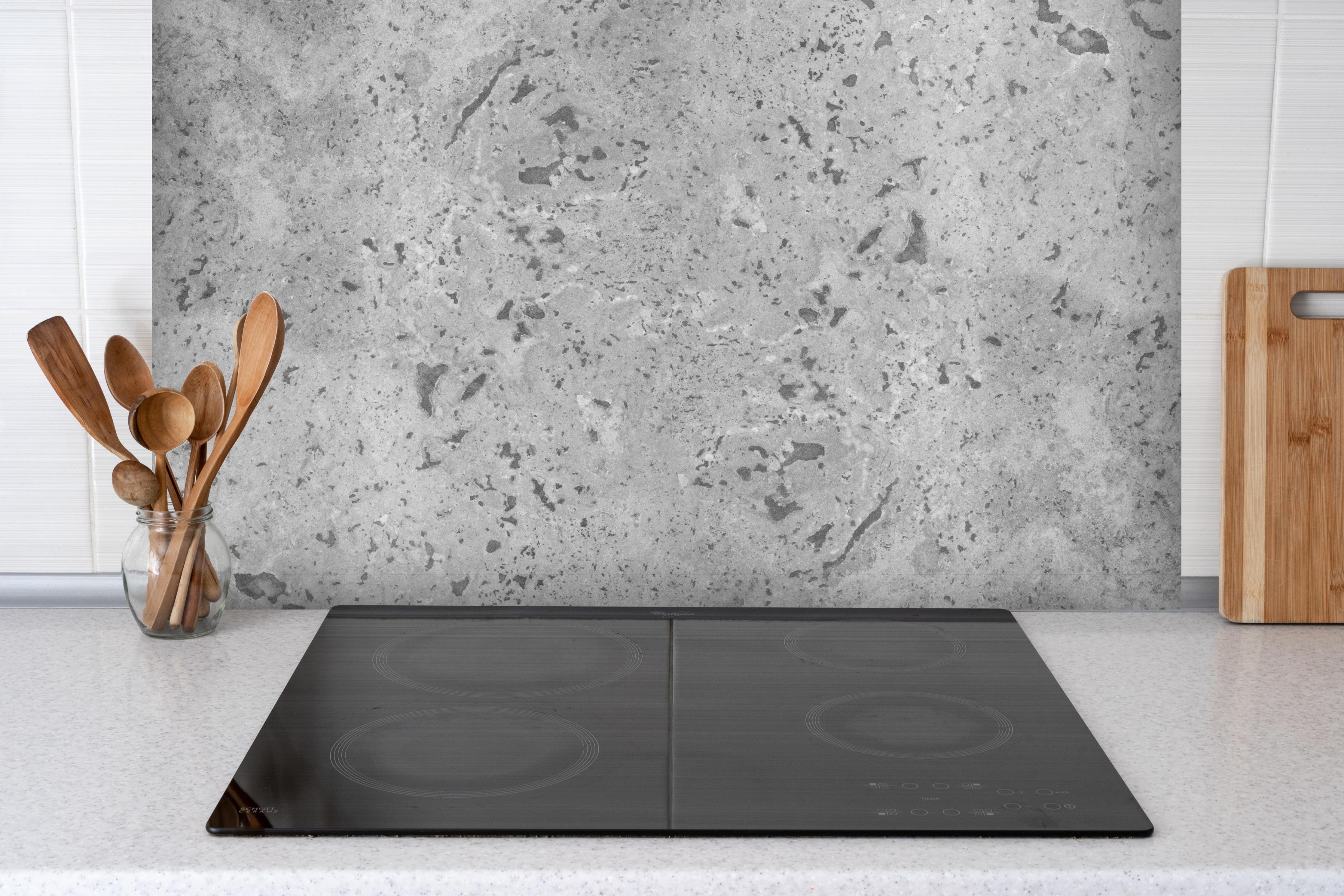 Spritzschutz - Grauer Beton hinter einem Cerankochfeld zwischen Holz-Kochutensilien