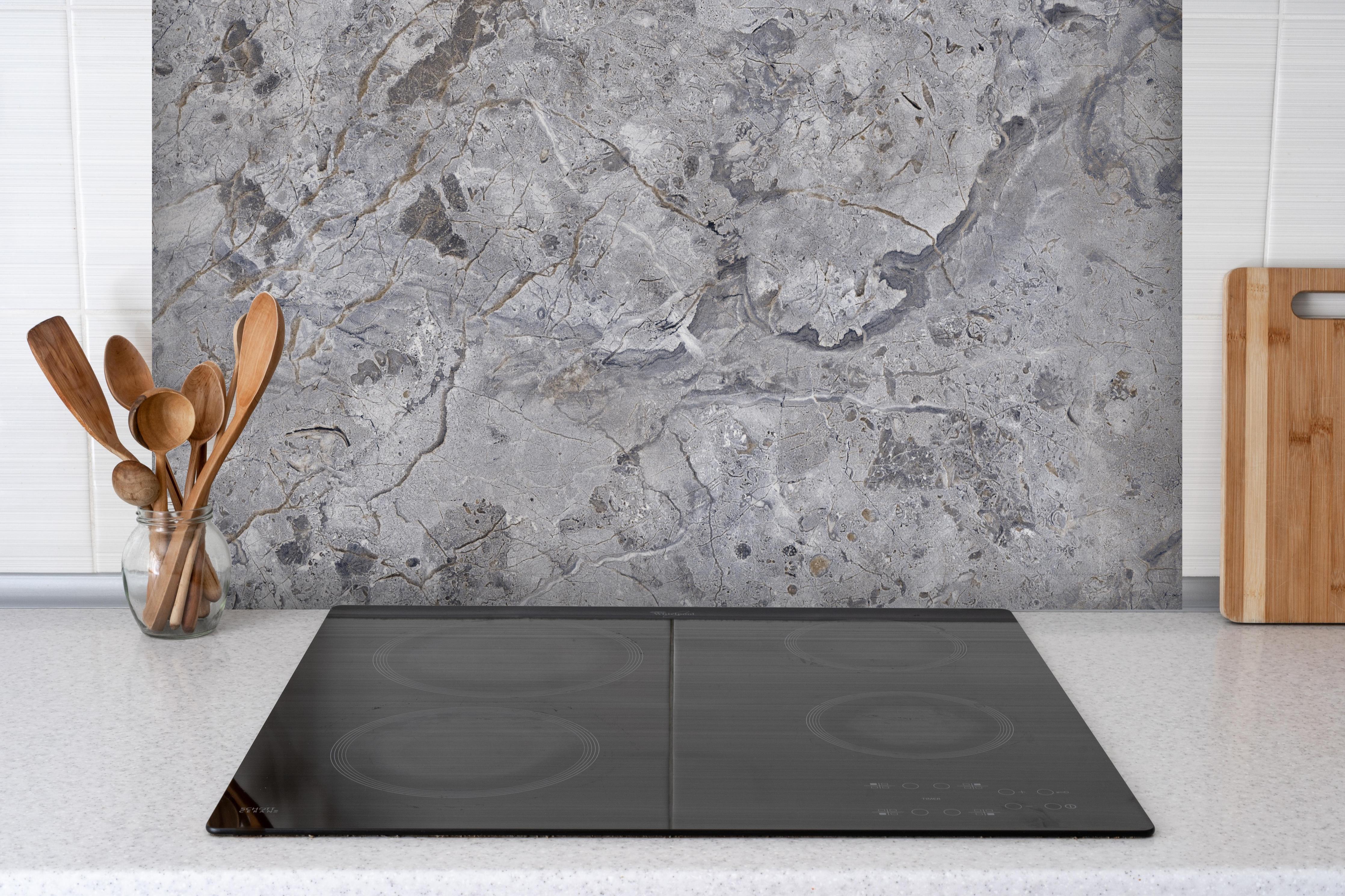 Spritzschutz - Grauer Marmor hinter einem Cerankochfeld zwischen Holz-Kochutensilien