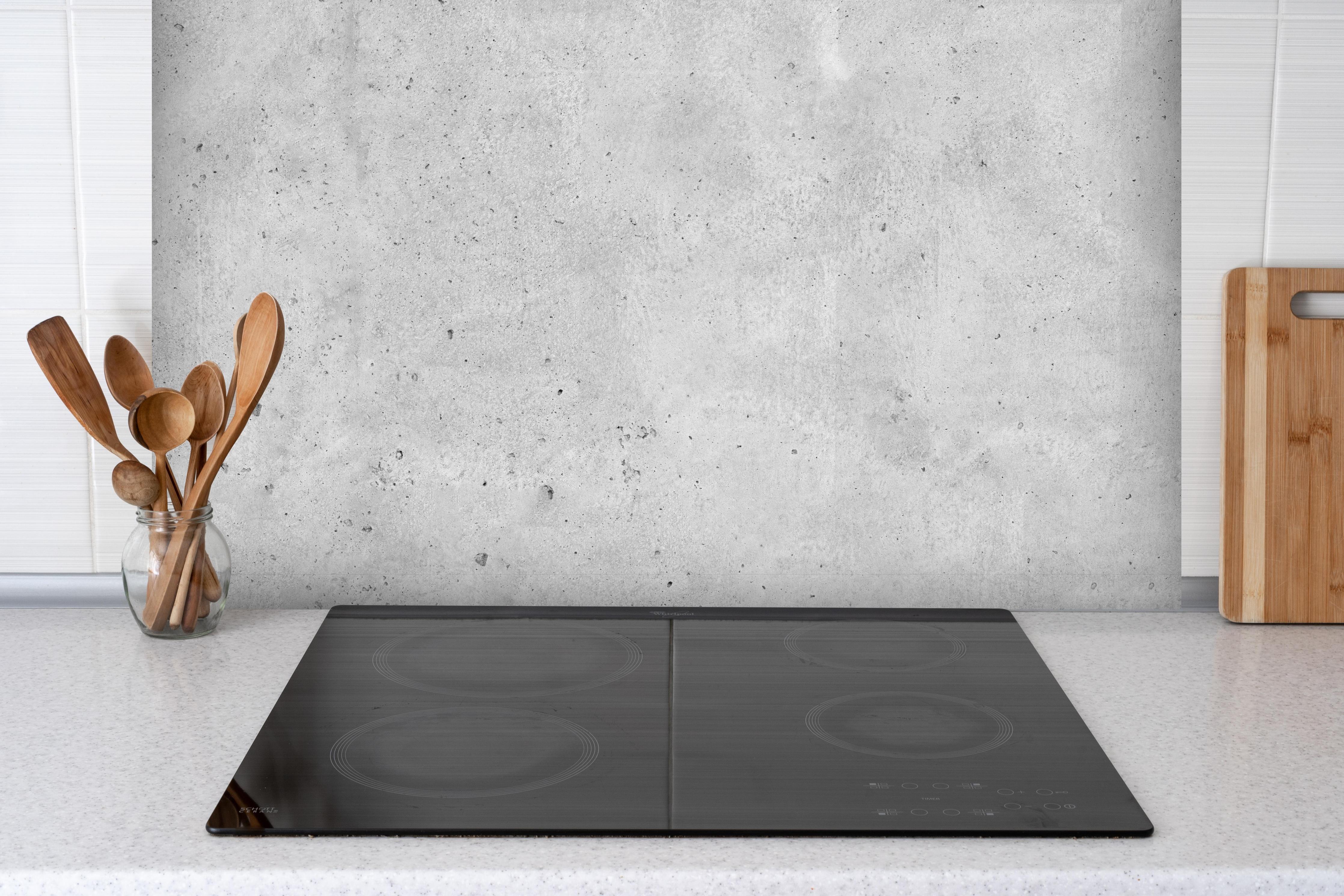 Spritzschutz - Grauer rauer Beton hinter einem Cerankochfeld zwischen Holz-Kochutensilien