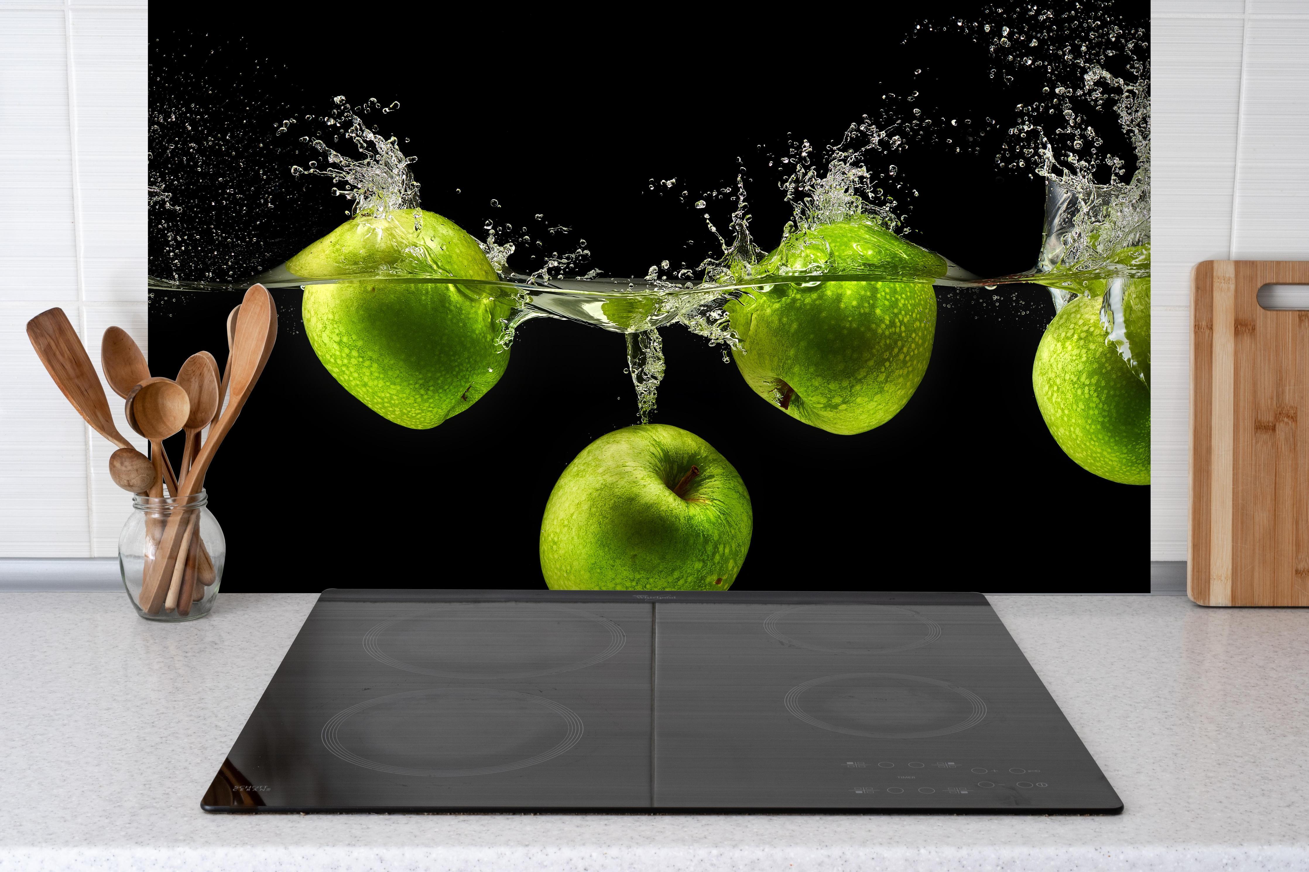 Spritzschutz - Grüne Äpfel im Wasser hinter einem Cerankochfeld zwischen Holz-Kochutensilien