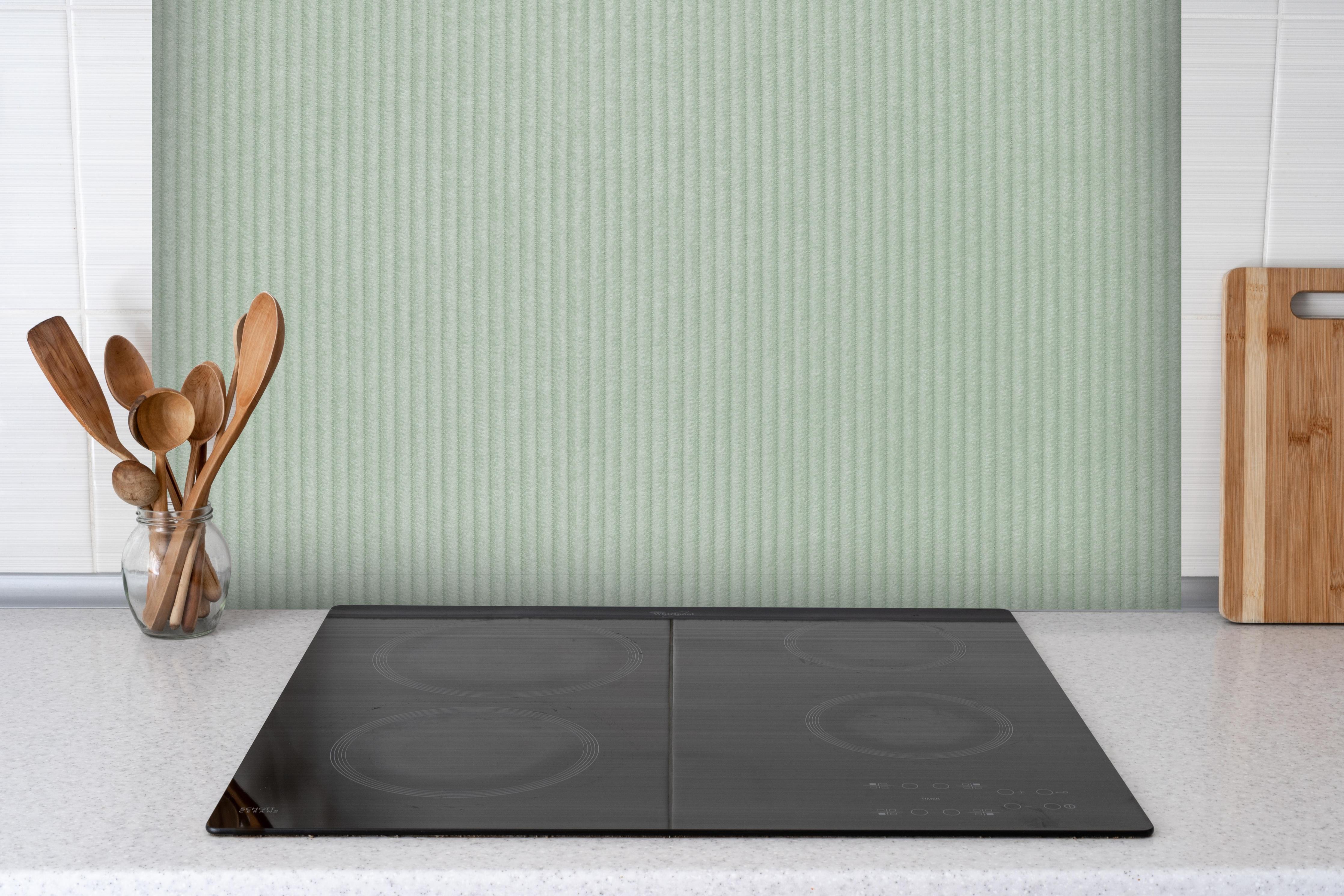 Spritzschutz - Grüner Stoff Textur hinter einem Cerankochfeld zwischen Holz-Kochutensilien