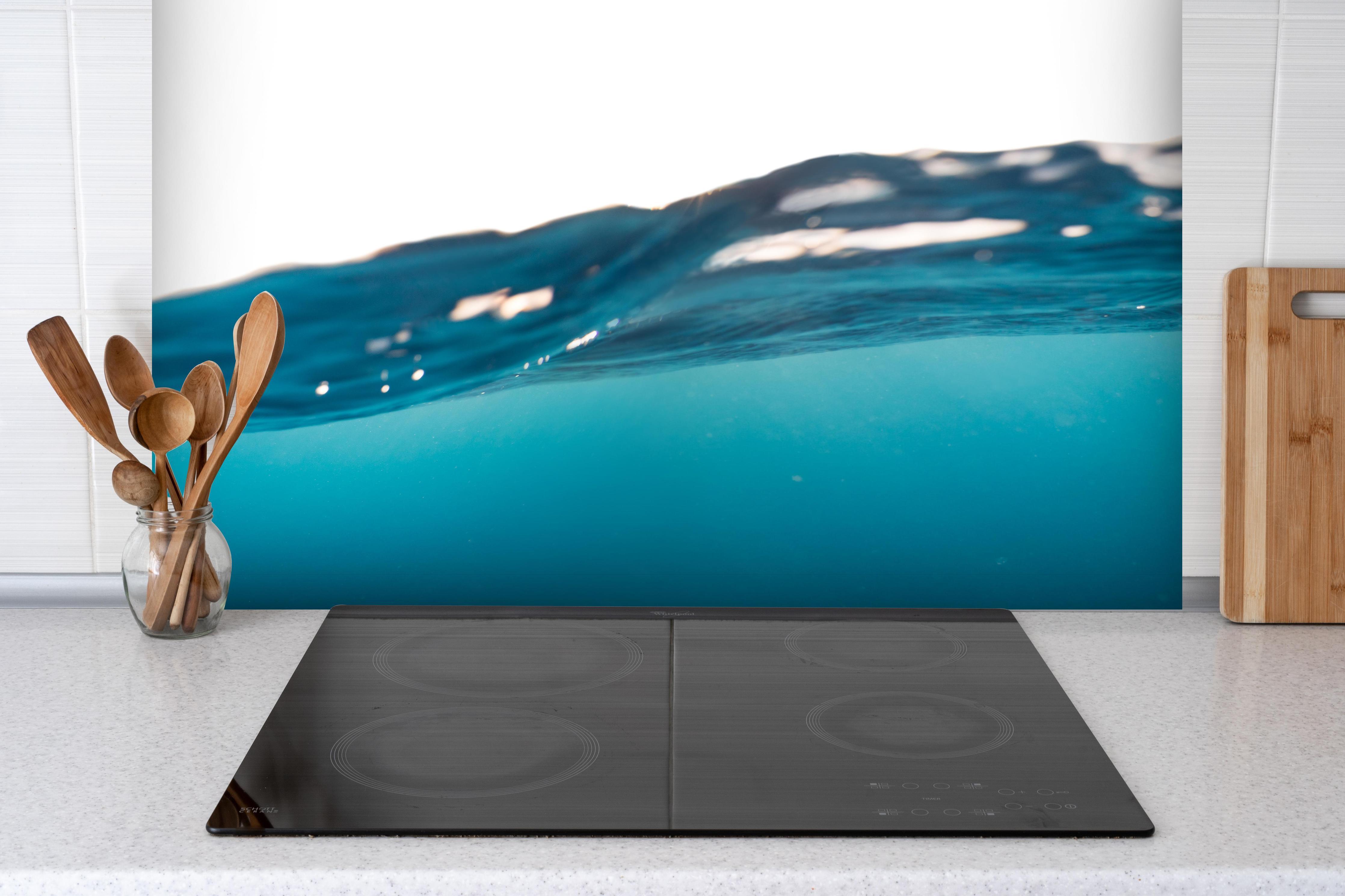 Spritzschutz - Harmonische Wasserwelle hinter einem Cerankochfeld zwischen Holz-Kochutensilien