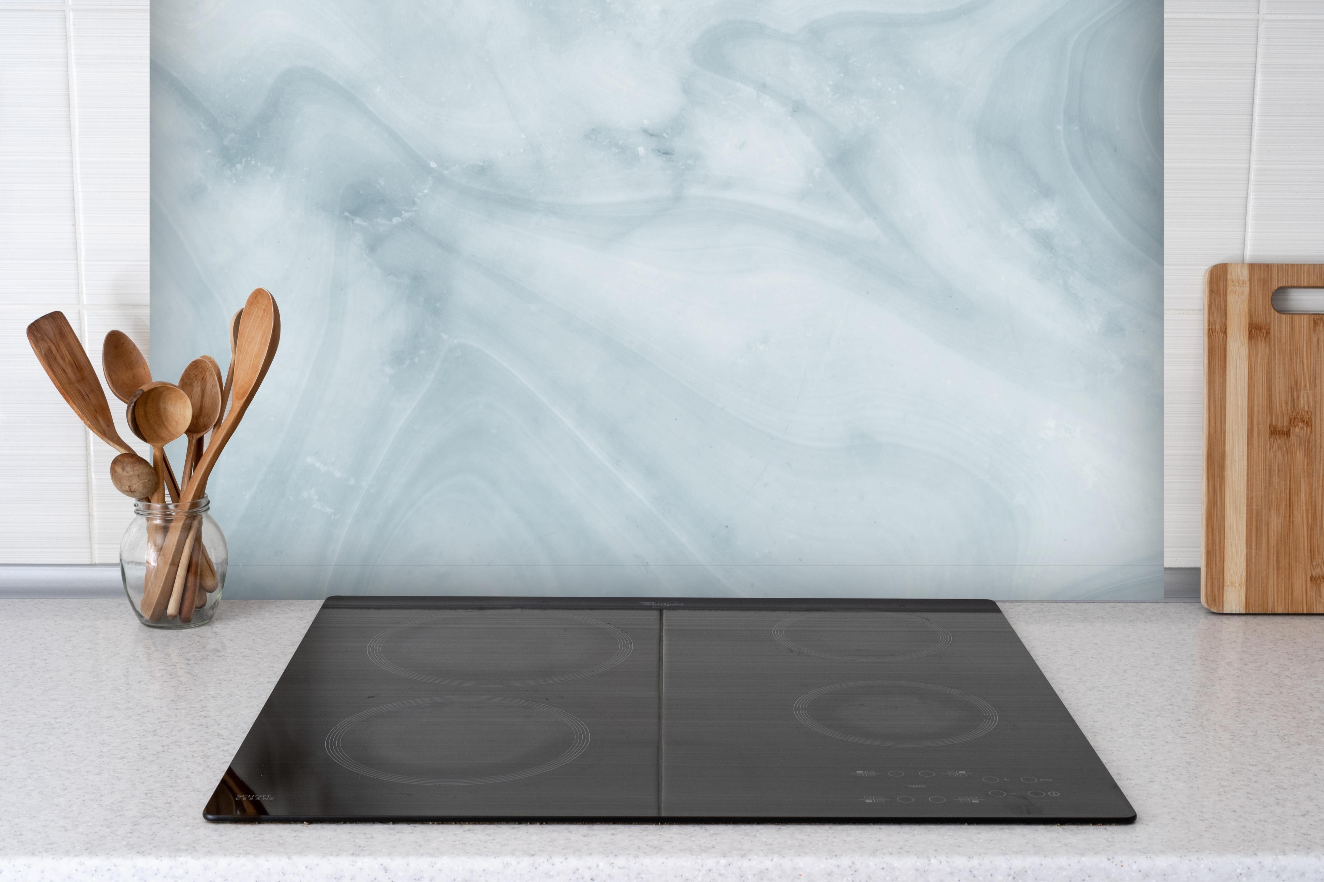 Spritzschutz - Helle bläuliche Marmor Textur hinter einem Cerankochfeld zwischen Holz-Kochutensilien