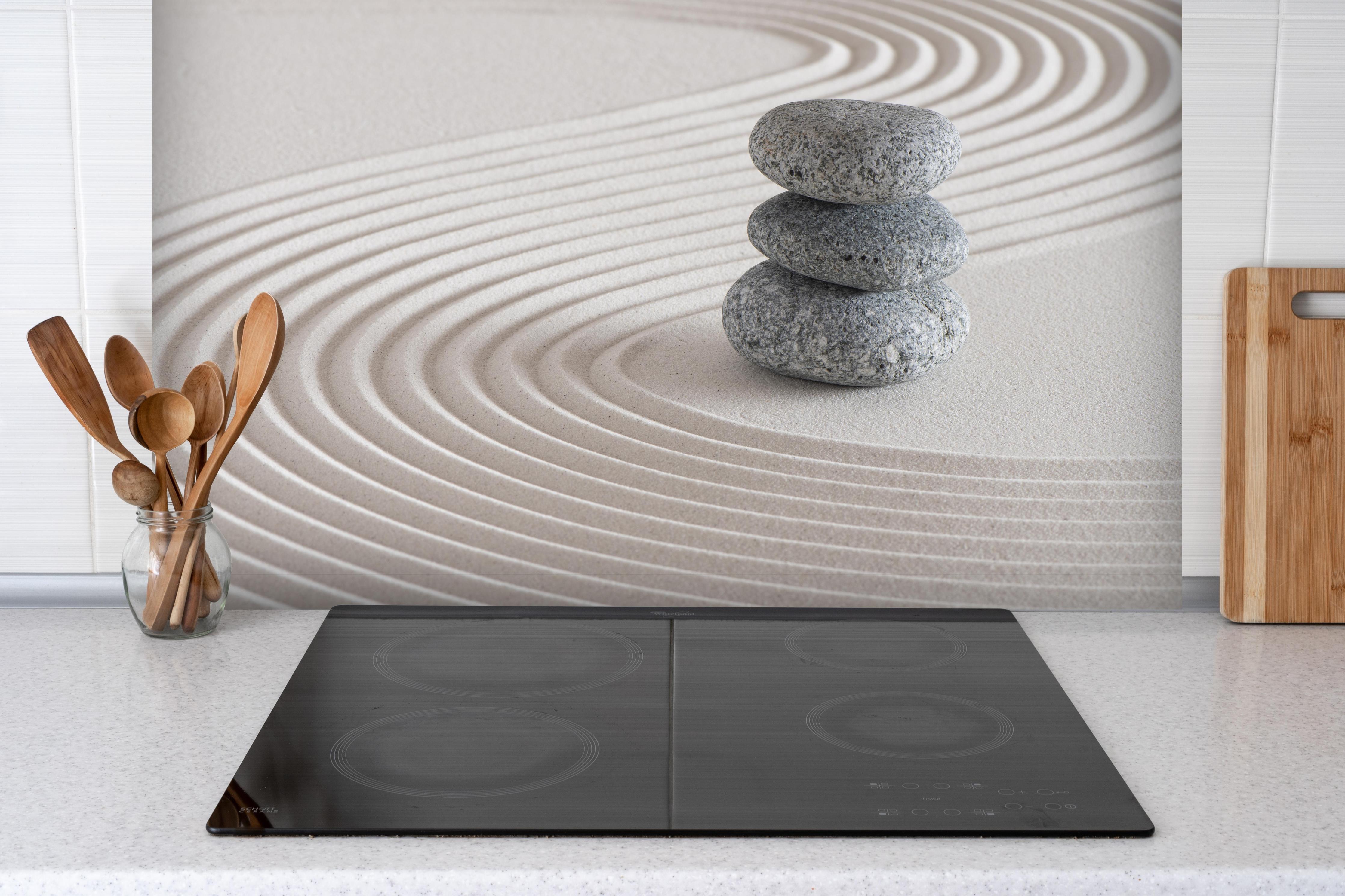 Spritzschutz - Japanischer Zen-Garten auf Sand hinter einem Cerankochfeld zwischen Holz-Kochutensilien