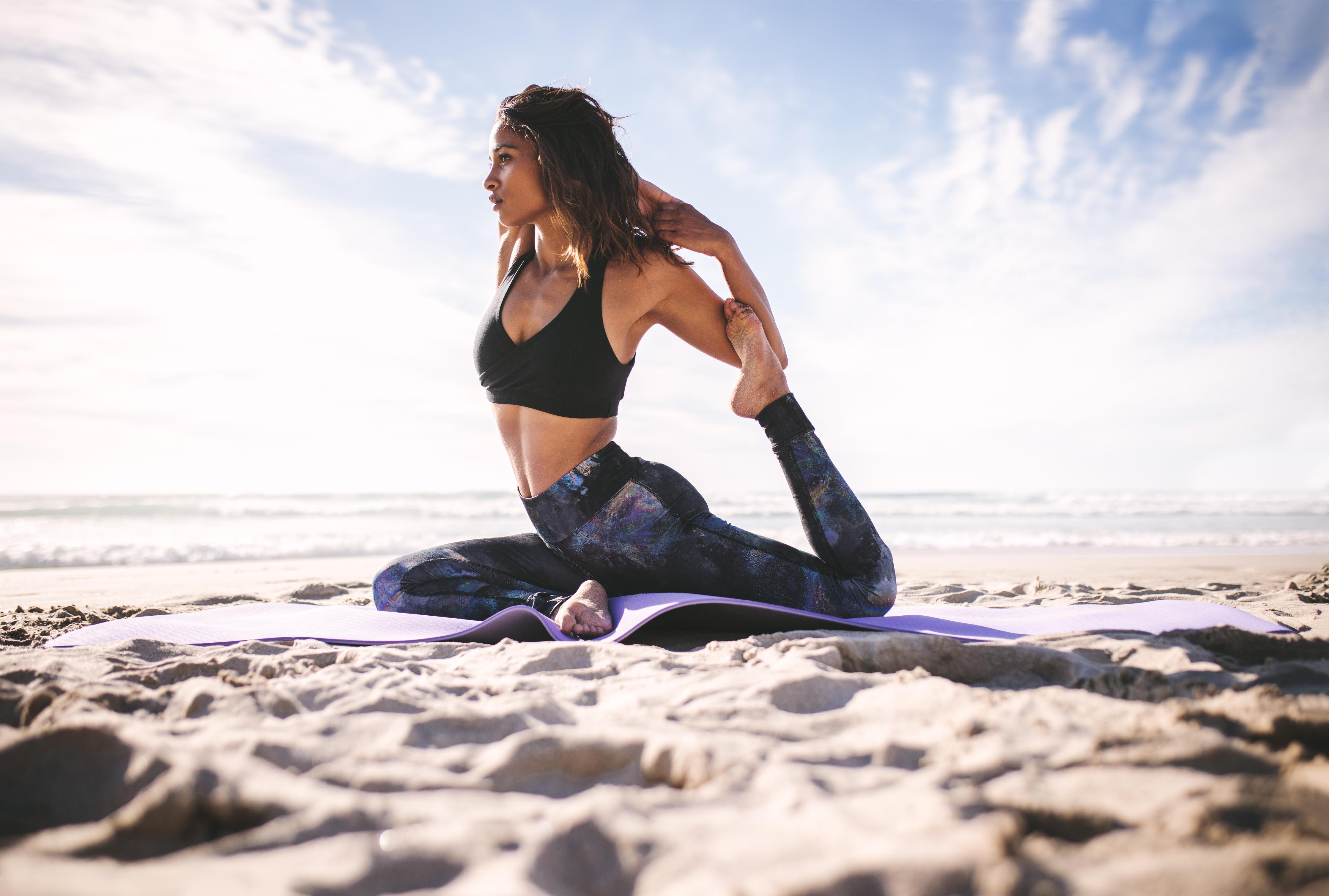 Spritzschutz-Junges Mädchen in King Pigeon Yoga Pose am Strand