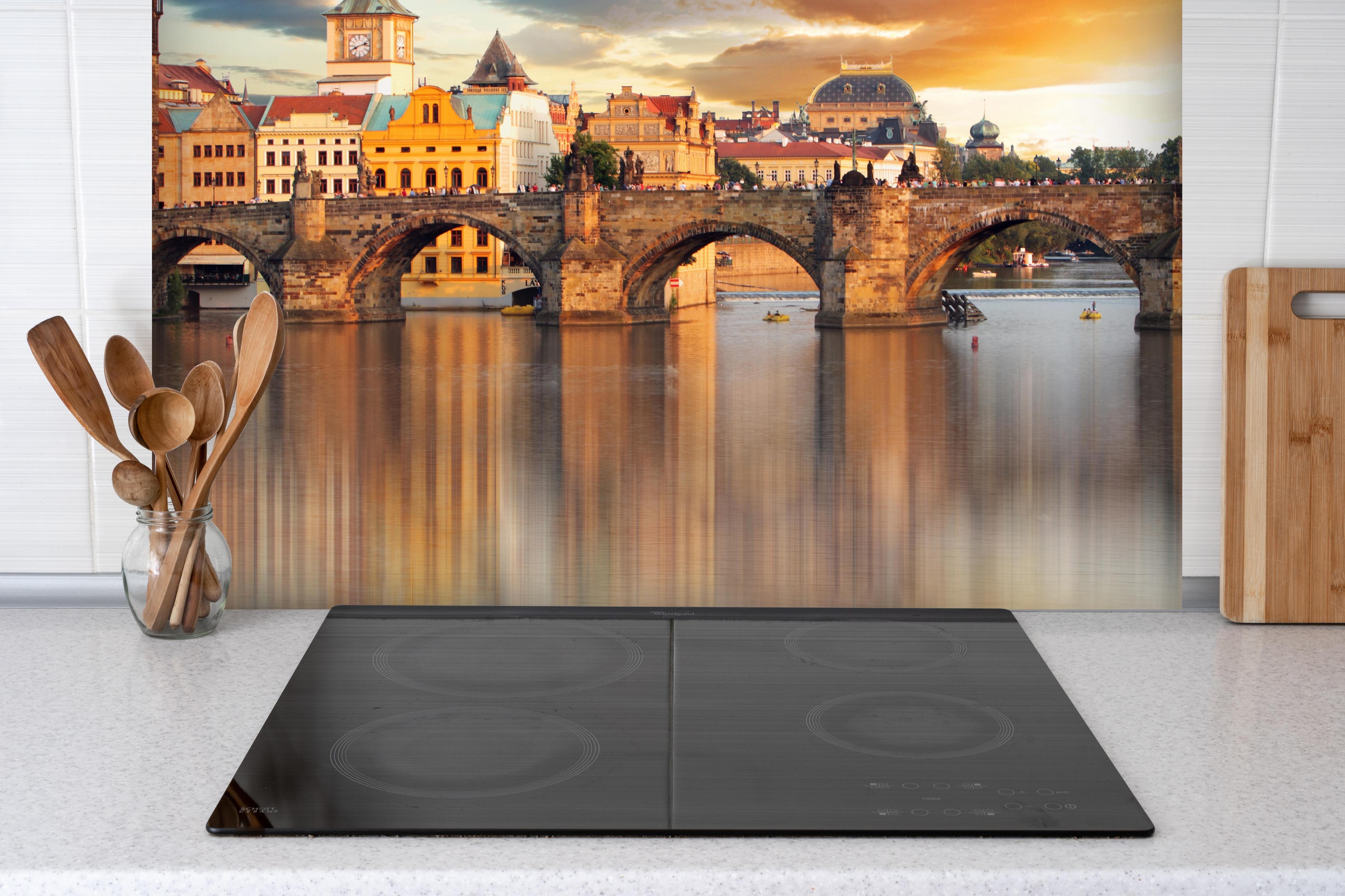 Spritzschutz - Karlsbrücke in Prag bei Sonnenuntergang hinter einem Cerankochfeld zwischen Holz-Kochutensilien