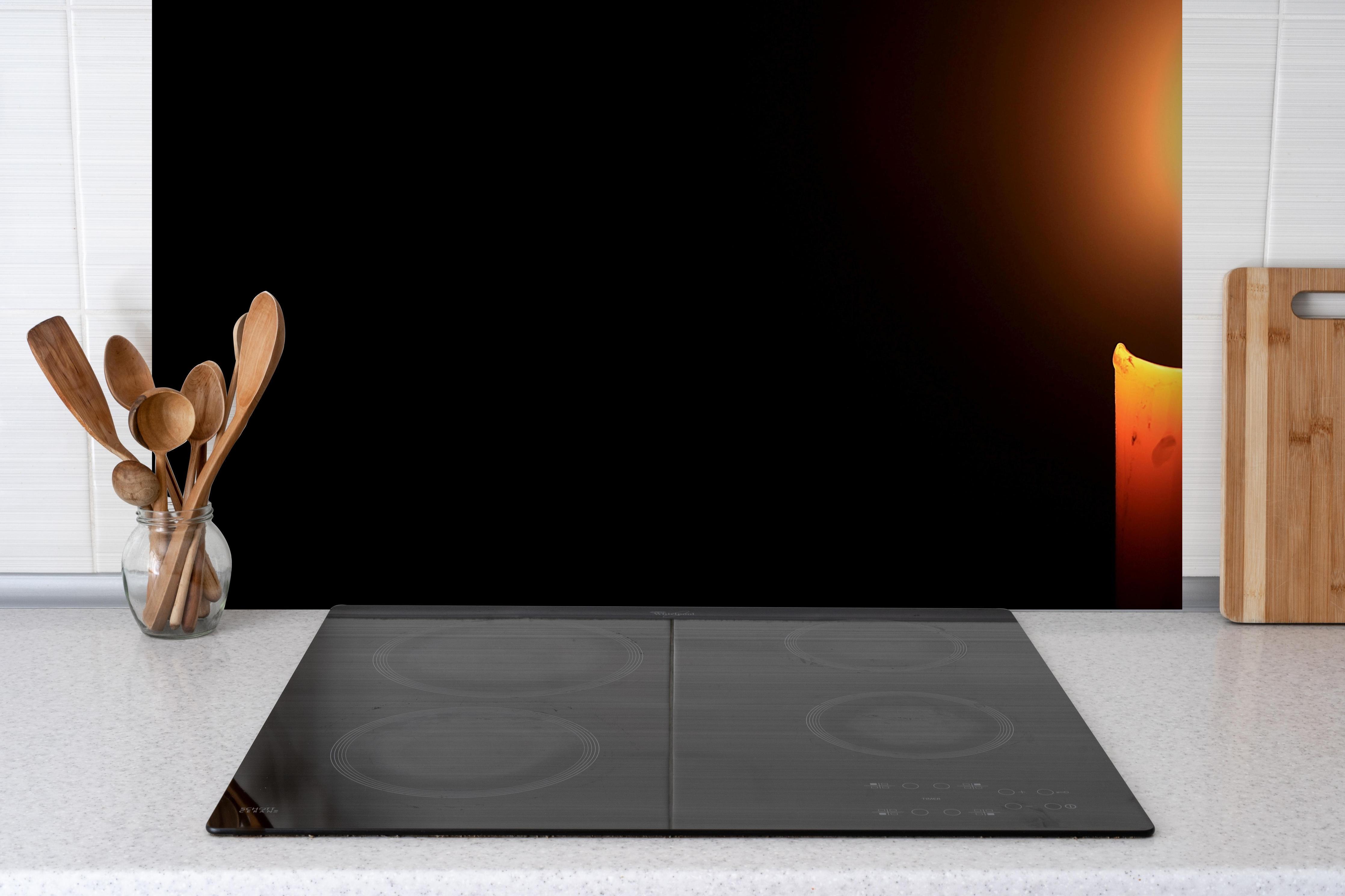 Spritzschutz - Kerzenlicht im Dunklen hinter einem Cerankochfeld zwischen Holz-Kochutensilien