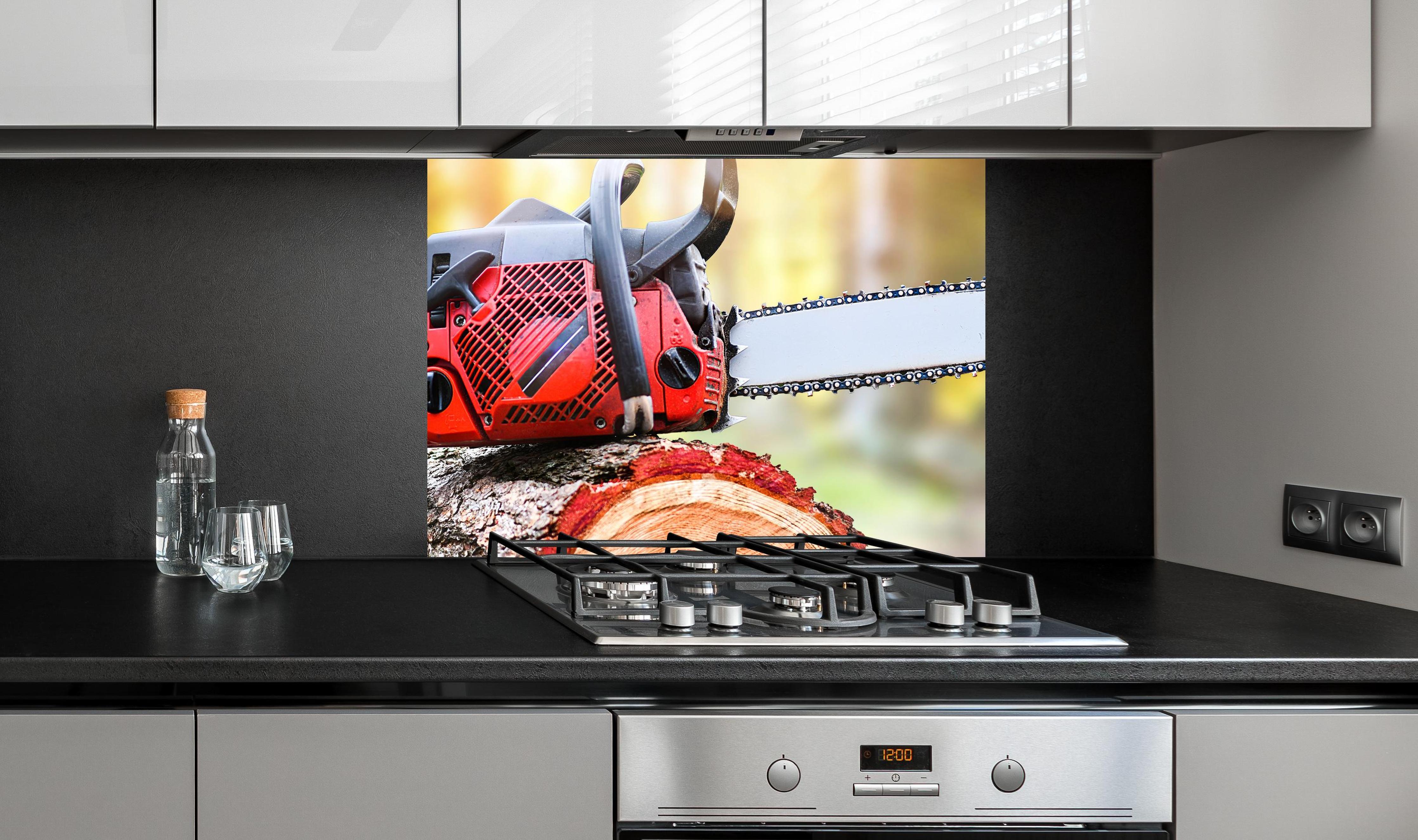 Spritzschutz - Kettensäge auf Holzstumpf an edler Anthrazit-Wand hinter silbernem Gasherd