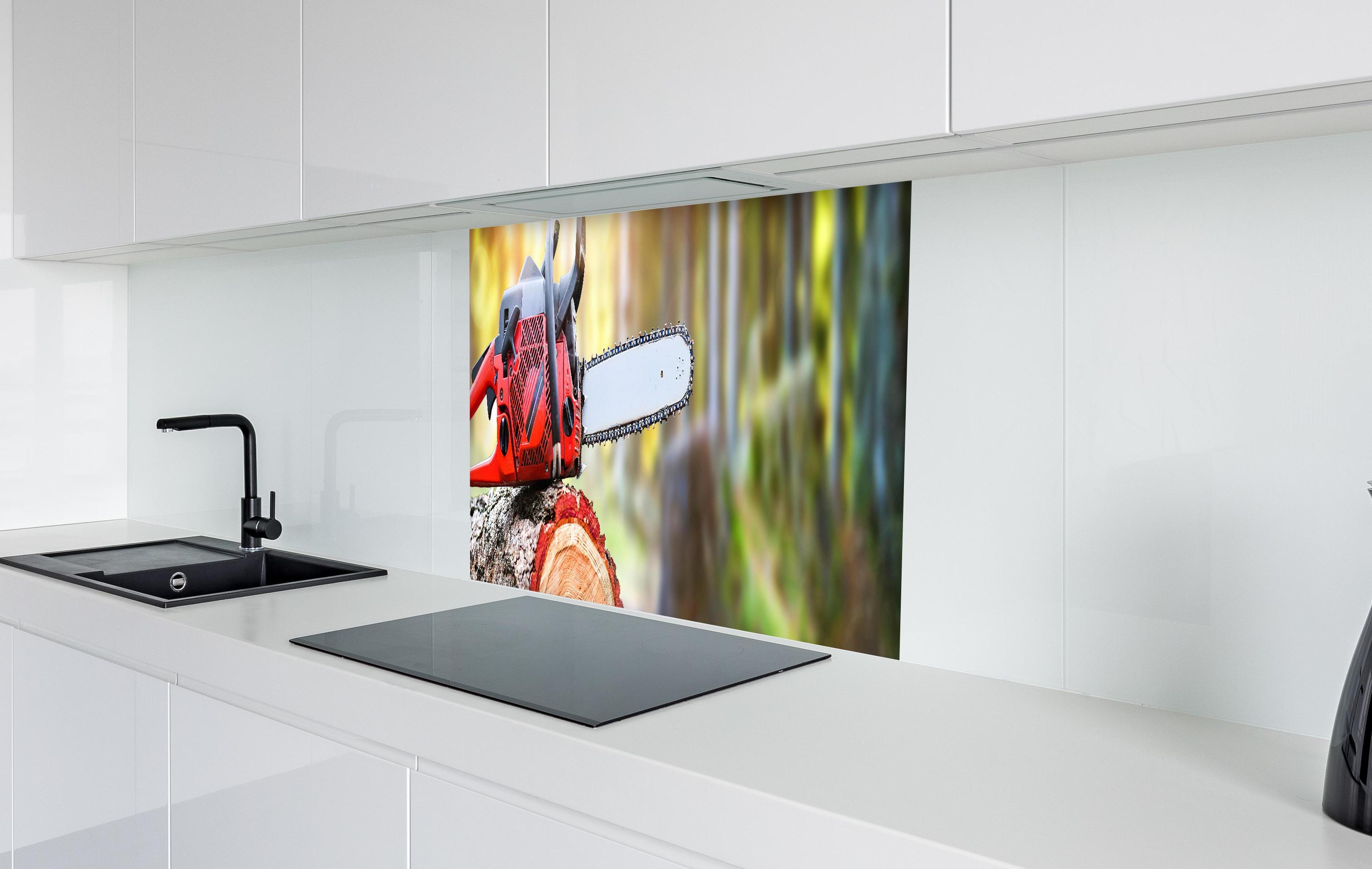 Spritzschutz - Kettensäge auf Holzstumpf in weißer Hochglanz-Küche hinter einem Cerankochfeld