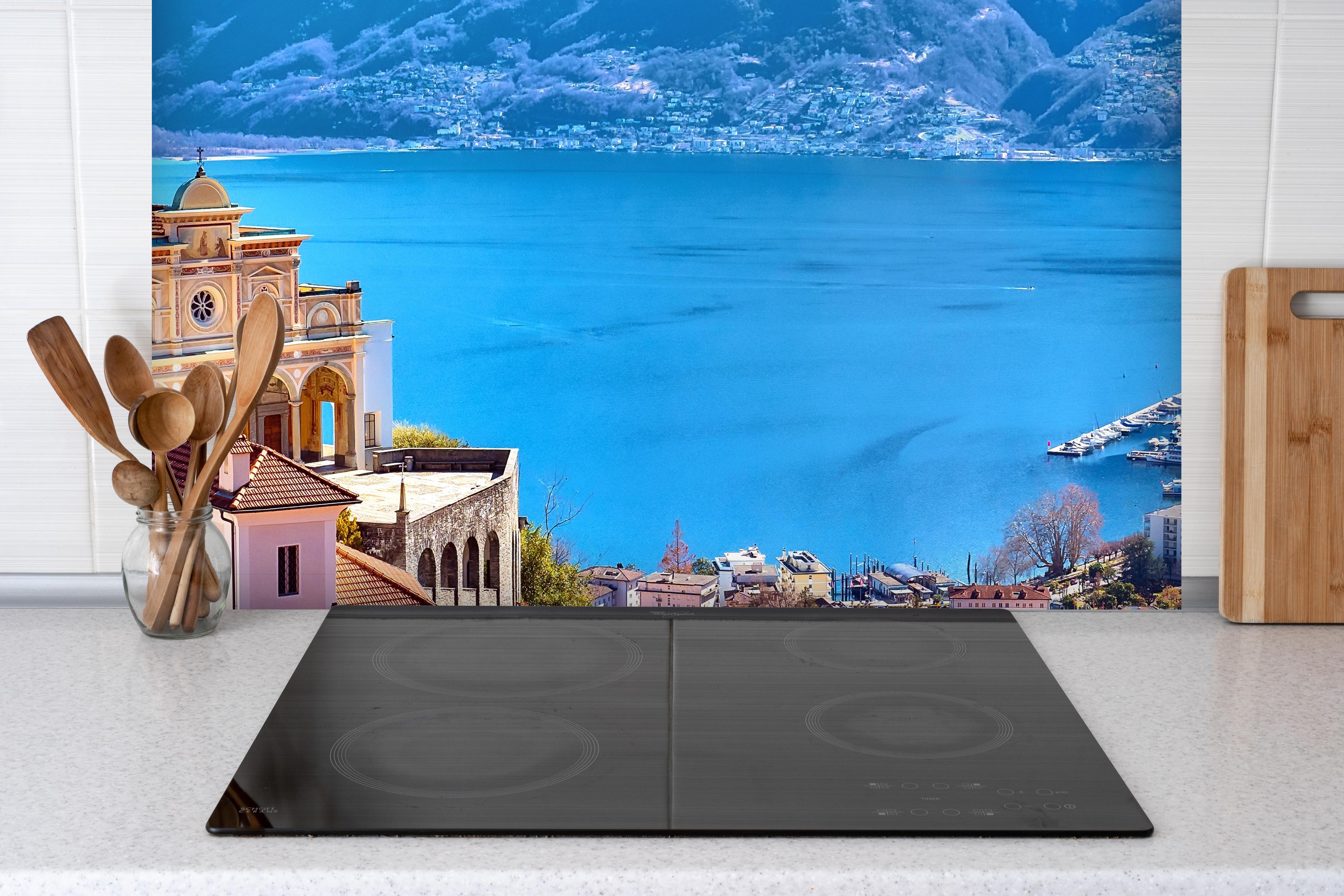 Spritzschutz - Kloster in Locarno hinter einem Cerankochfeld zwischen Holz-Kochutensilien