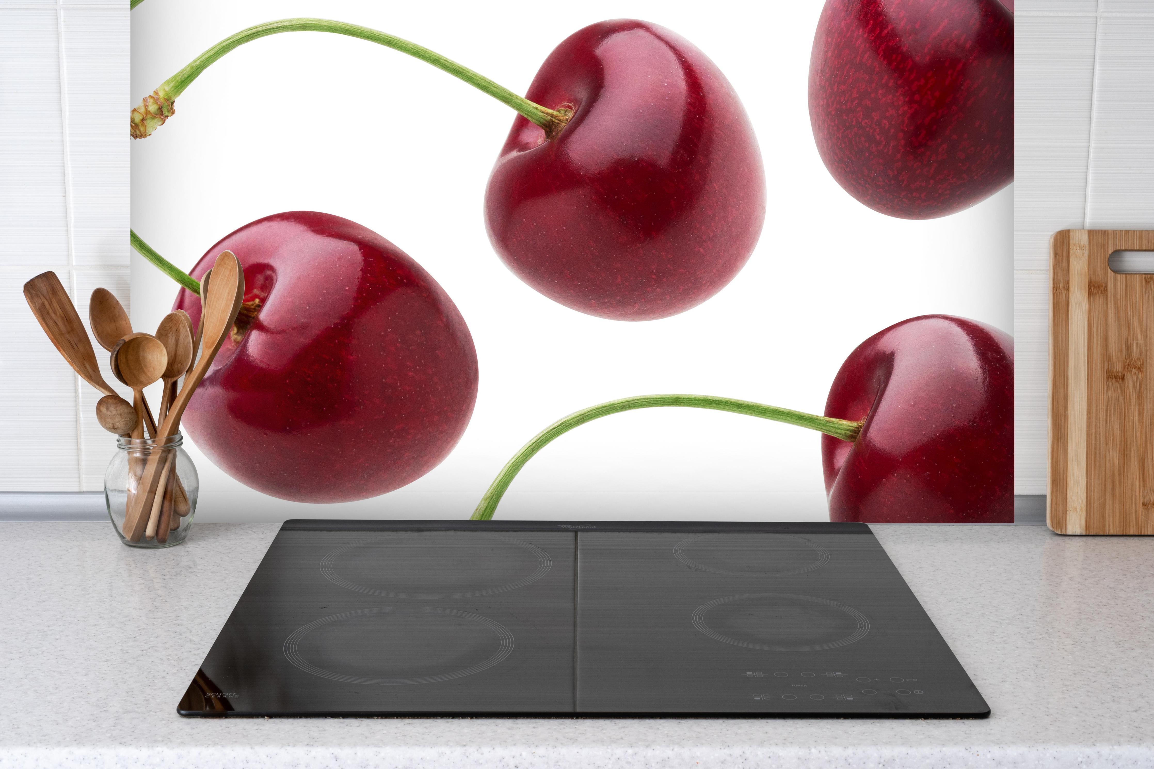 Spritzschutz - Knackige dunkelrote Kirchen hinter einem Cerankochfeld zwischen Holz-Kochutensilien