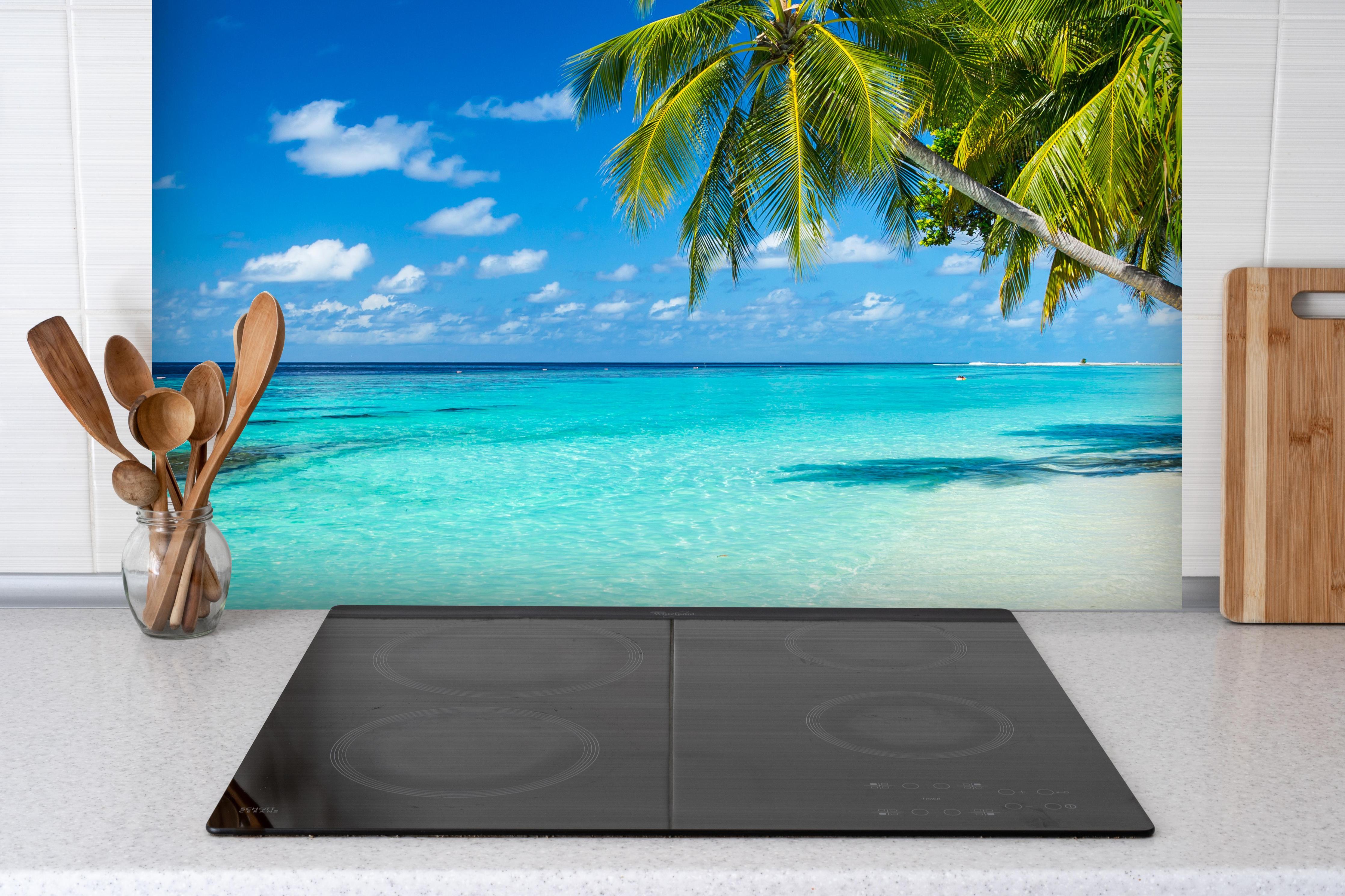 Spritzschutz - Kokospalmen am Strand in der Karibik hinter einem Cerankochfeld zwischen Holz-Kochutensilien