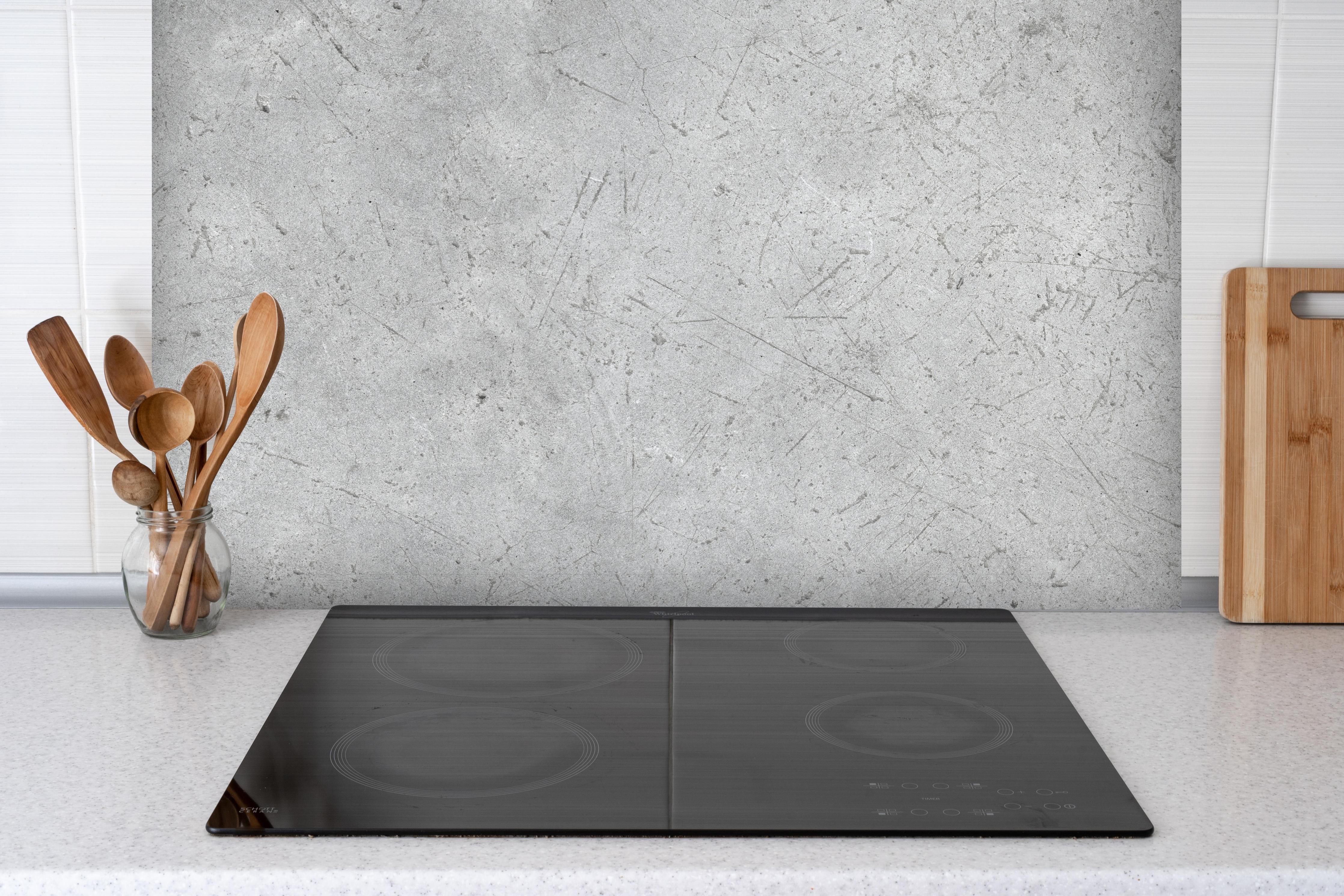 Spritzschutz - Kratzige graue Betonwand hinter einem Cerankochfeld zwischen Holz-Kochutensilien