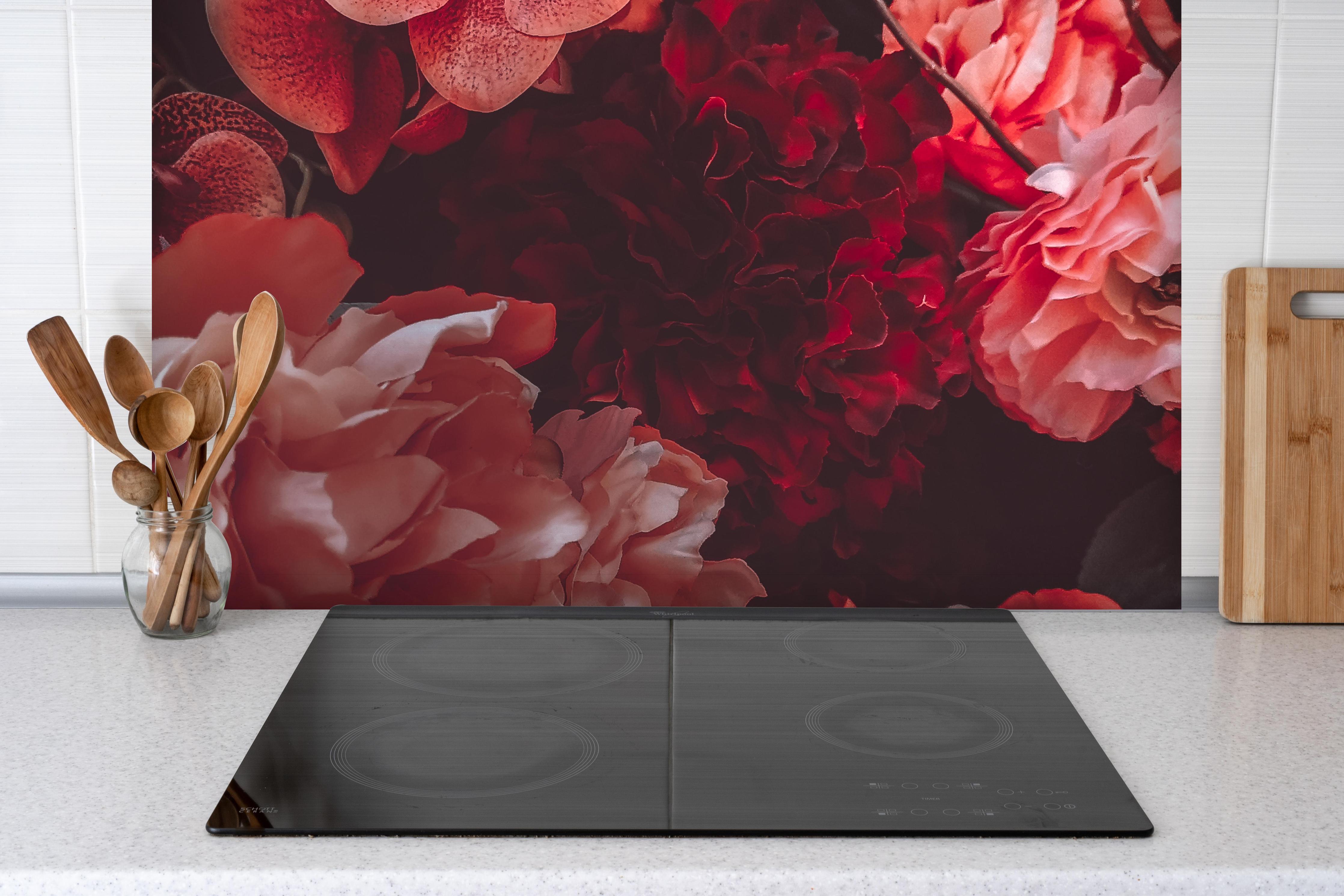 Spritzschutz - Künstliche rötliche Blumen hinter einem Cerankochfeld zwischen Holz-Kochutensilien