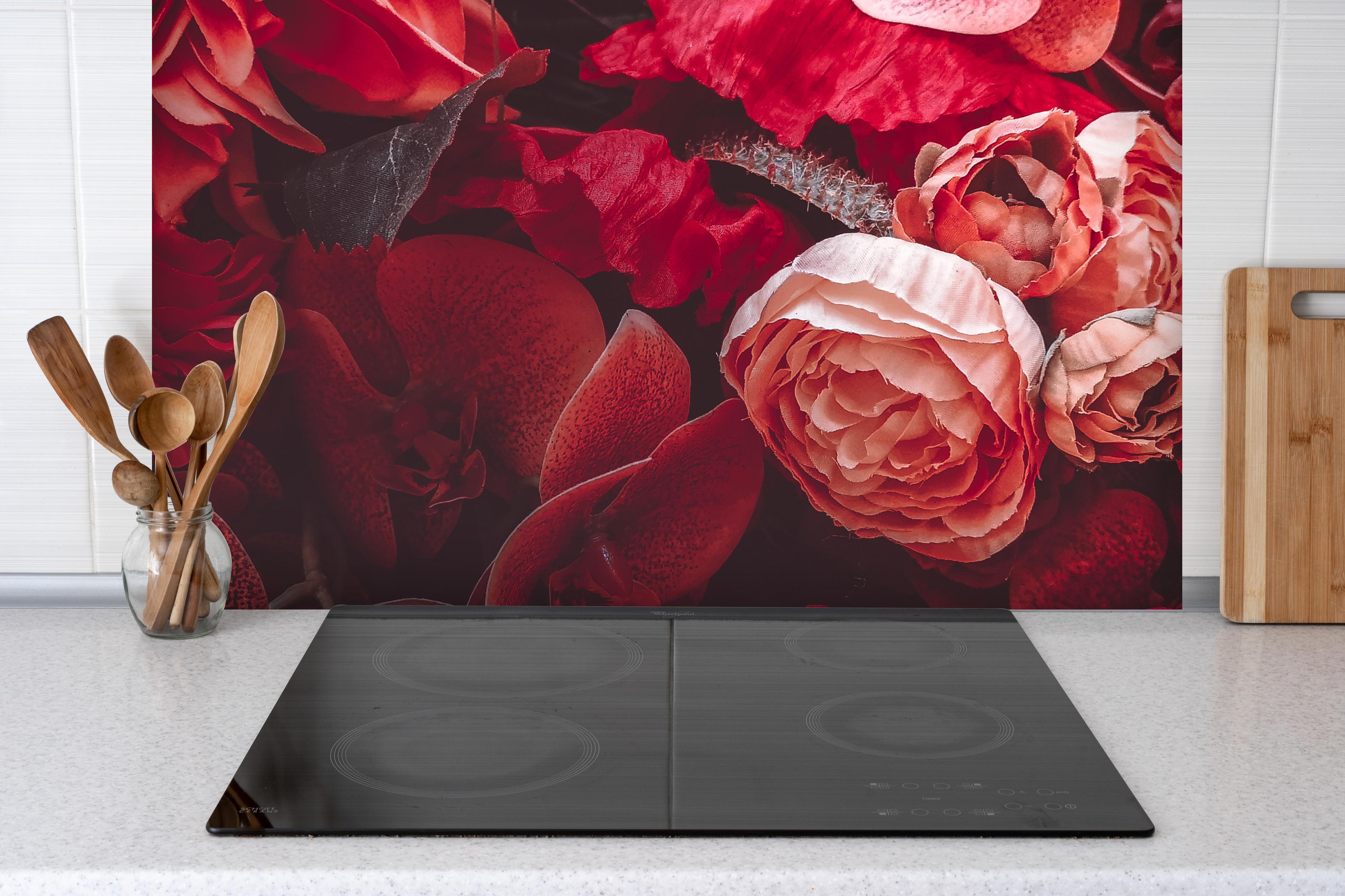 Spritzschutz - Künstliche rötliche Blumen hinter einem Cerankochfeld zwischen Holz-Kochutensilien