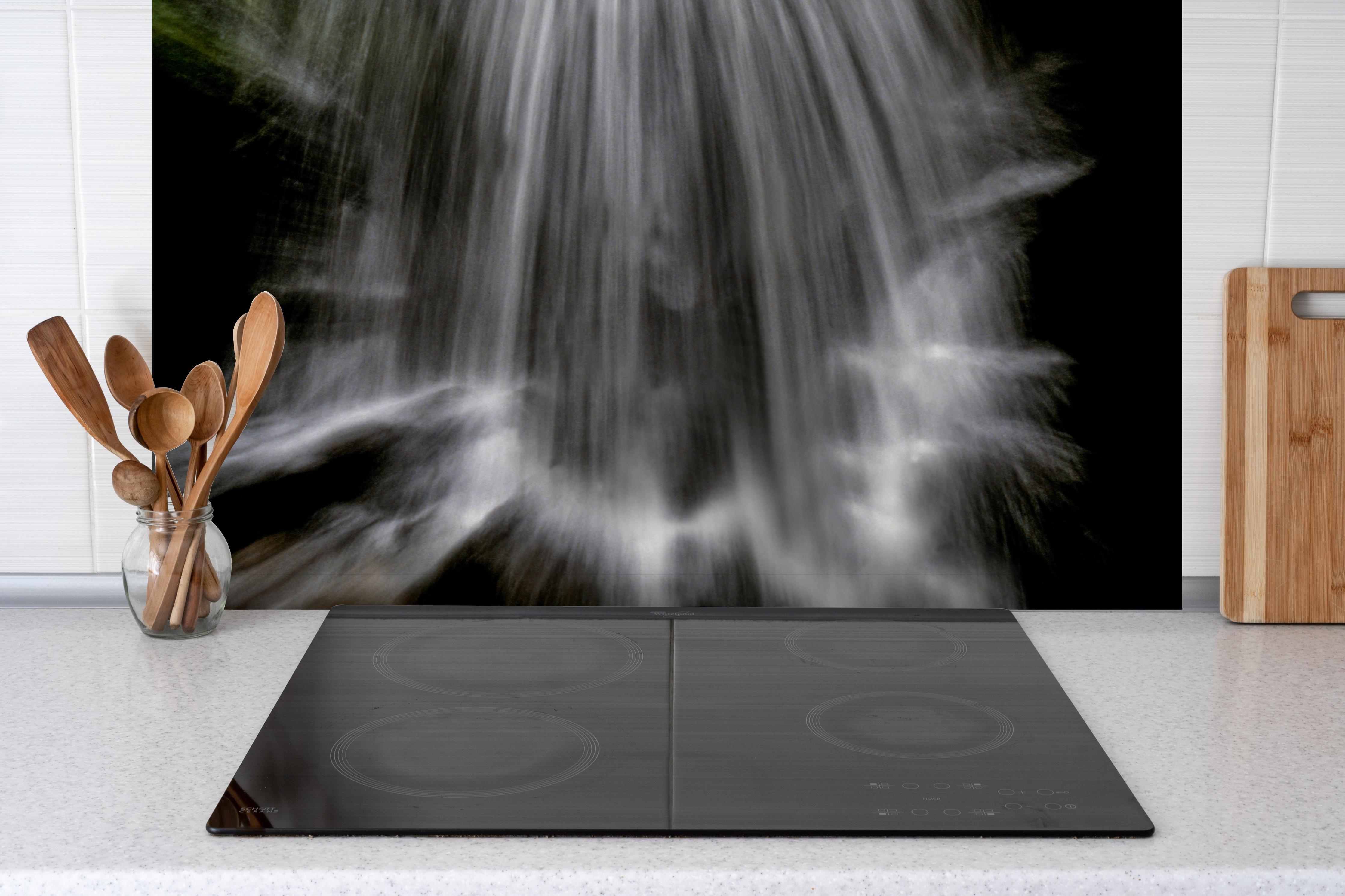 Spritzschutz - Kunstvoller Wasserfall hinter einem Cerankochfeld zwischen Holz-Kochutensilien