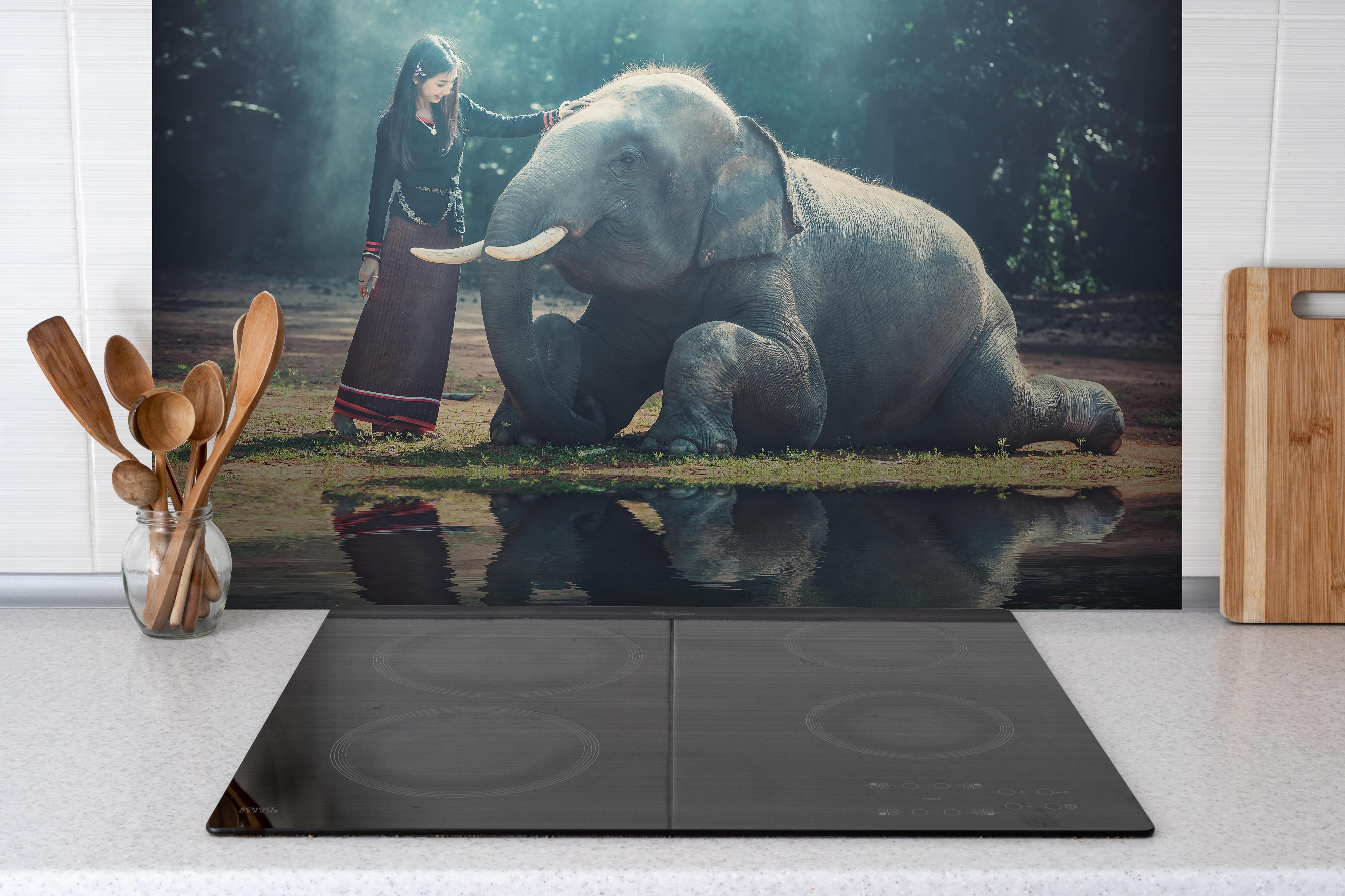 Spritzschutz - Mädchen mit lächelndem Elefanten in Asien hinter einem Cerankochfeld zwischen Holz-Kochutensilien
