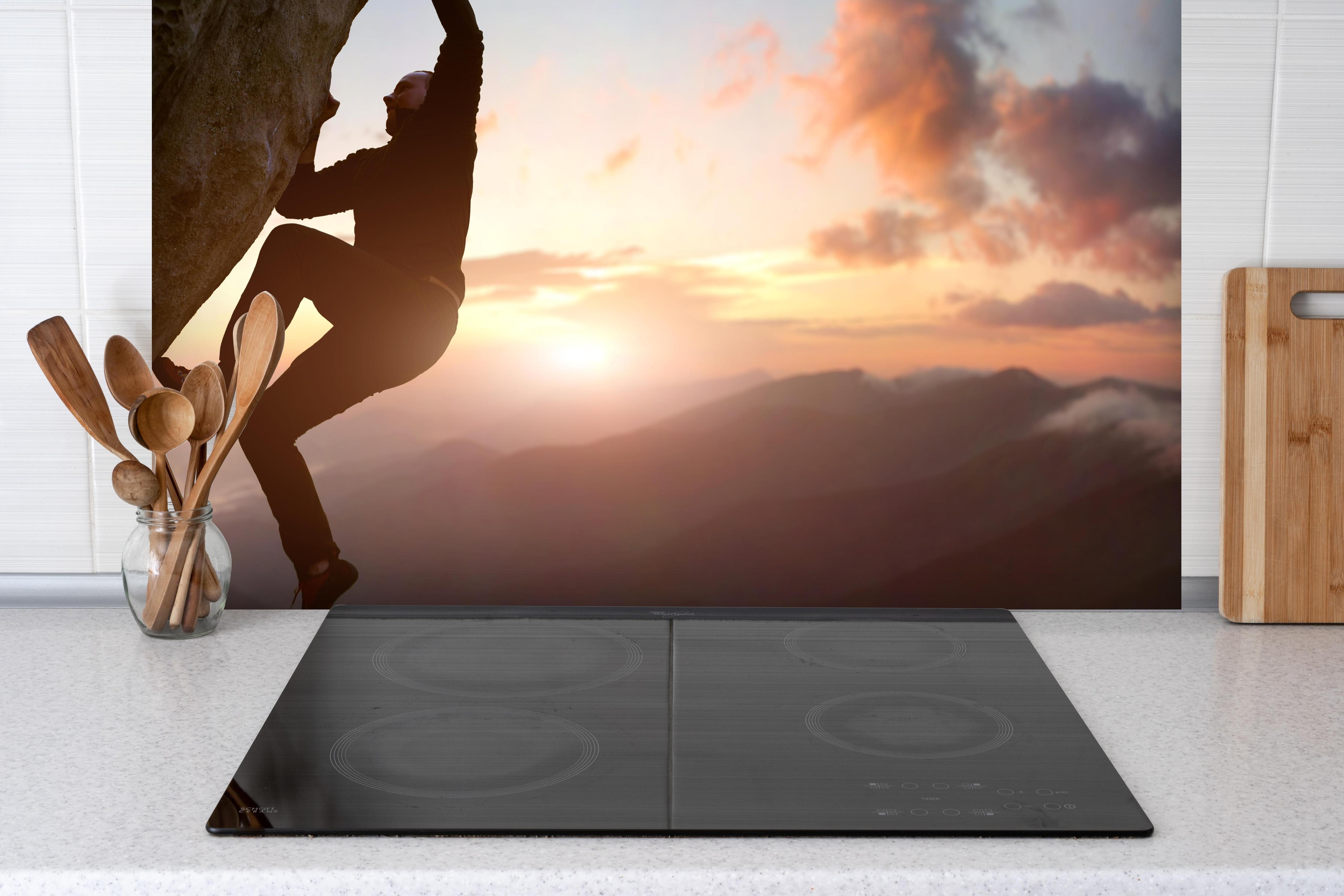 Spritzschutz - Männlicher Kletterer bei Sonnenuntergang hinter einem Cerankochfeld zwischen Holz-Kochutensilien