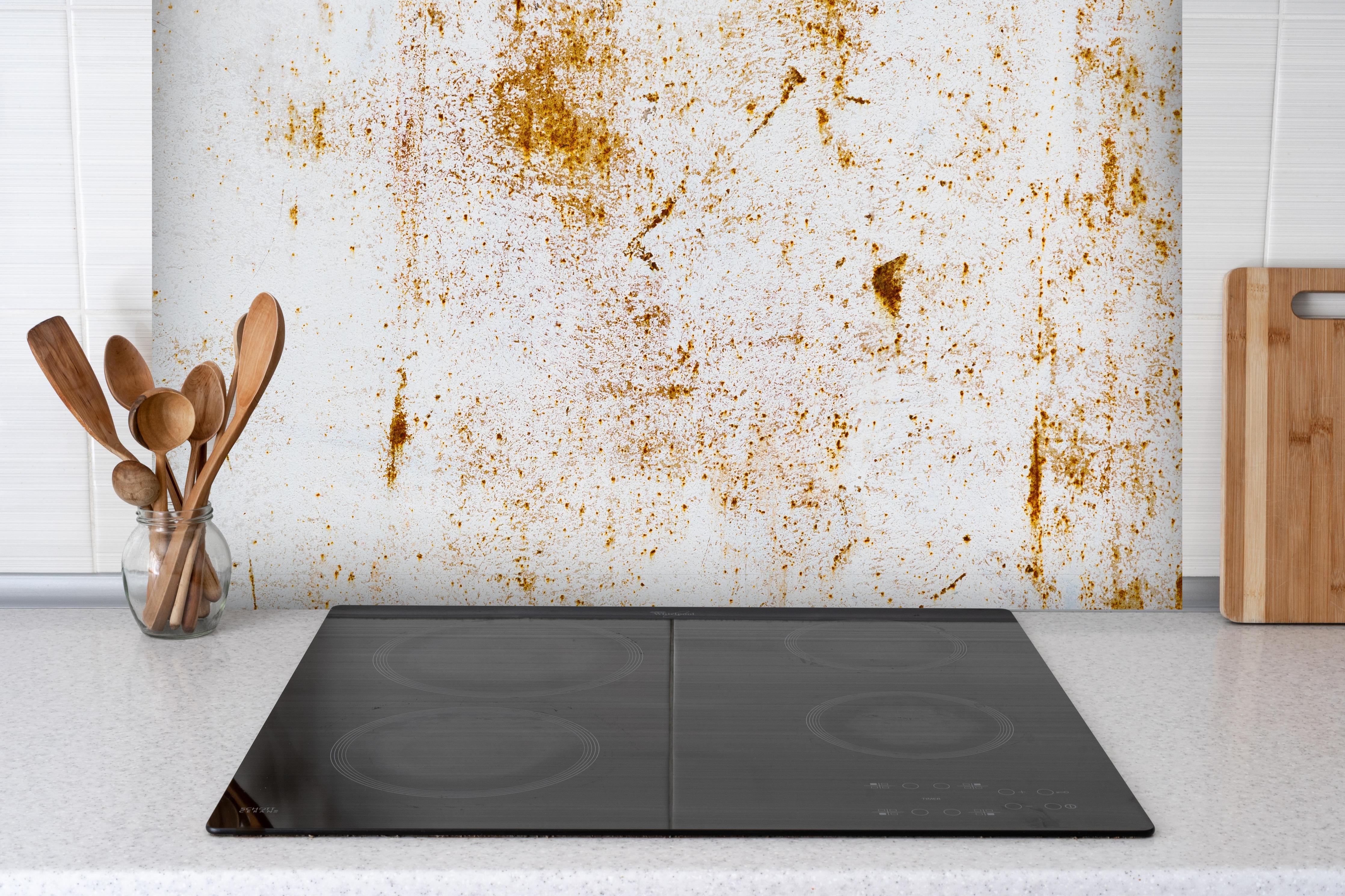 Spritzschutz - Metall mit rauer Rostoberfläche hinter einem Cerankochfeld zwischen Holz-Kochutensilien