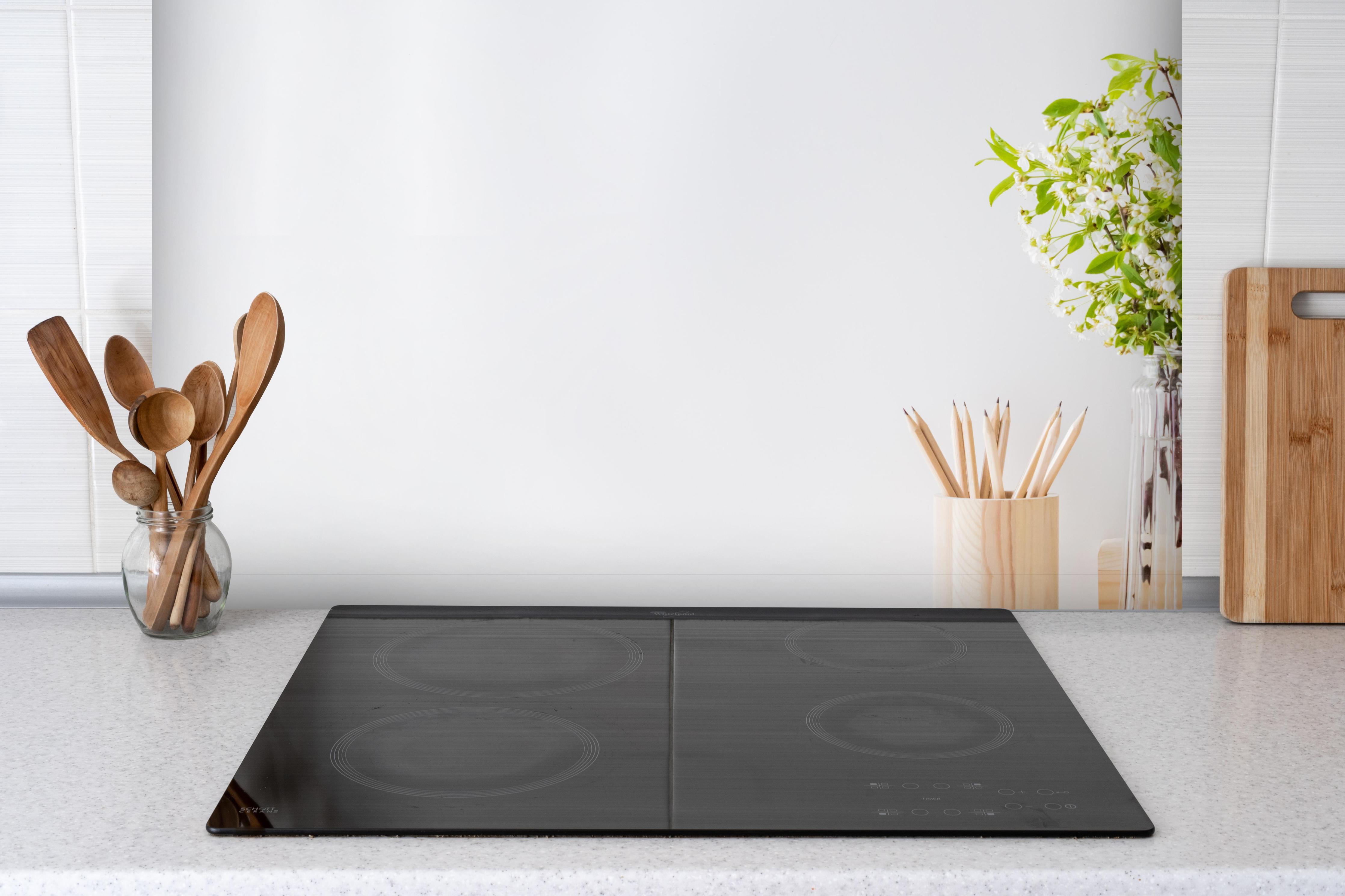 Spritzschutz - Minimalistischer weißer Bürotisch hinter einem Cerankochfeld zwischen Holz-Kochutensilien