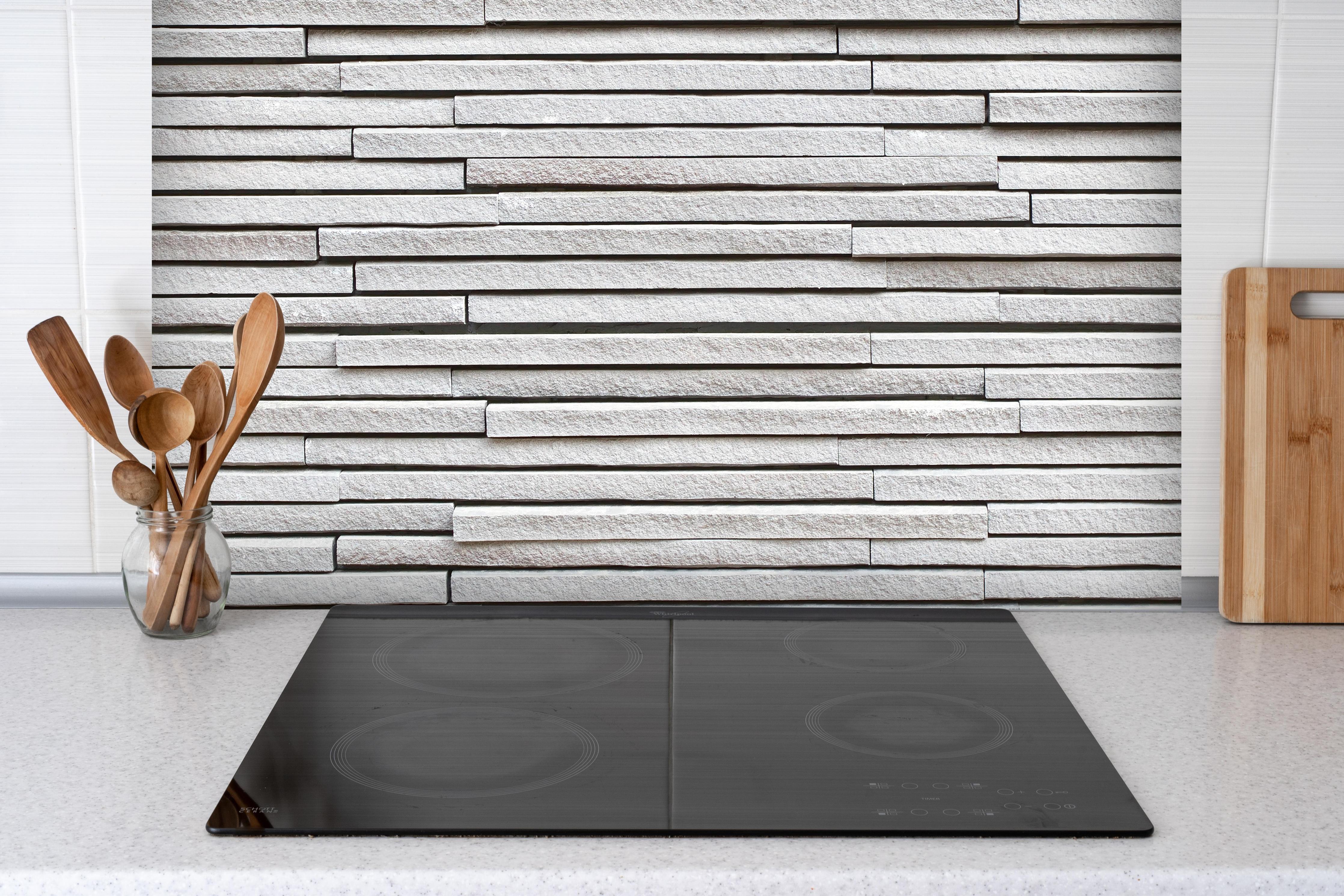 Spritzschutz - Moderne helle Steinwand hinter einem Cerankochfeld zwischen Holz-Kochutensilien