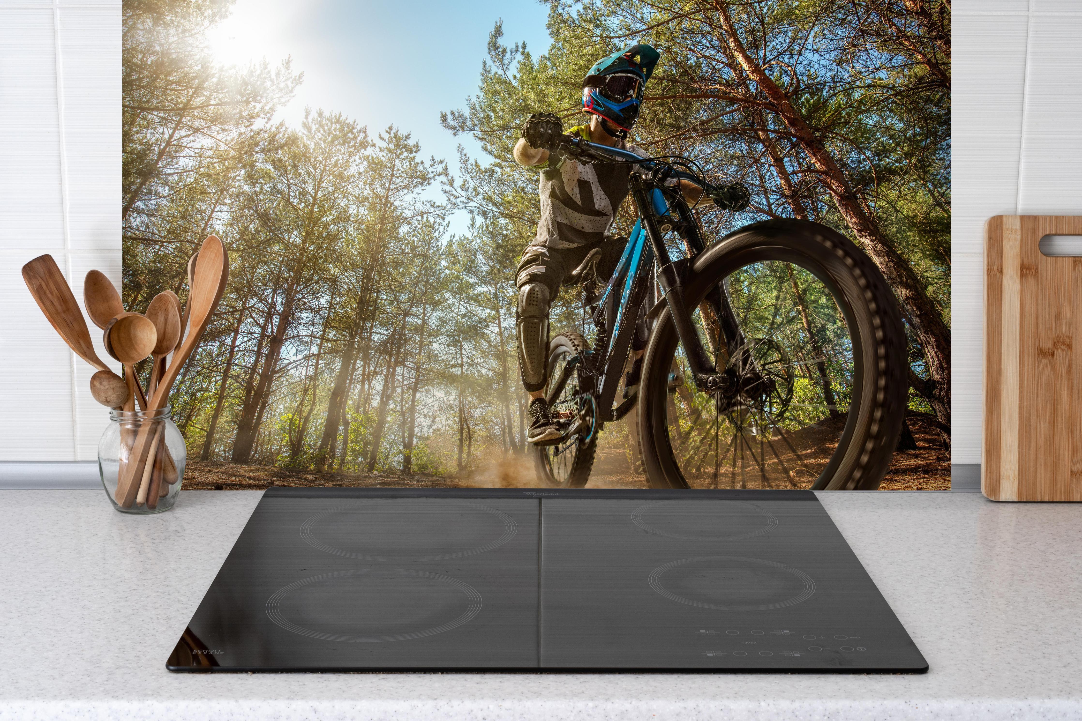 Spritzschutz - Mountainbiker auf Waldweg hinter einem Cerankochfeld zwischen Holz-Kochutensilien