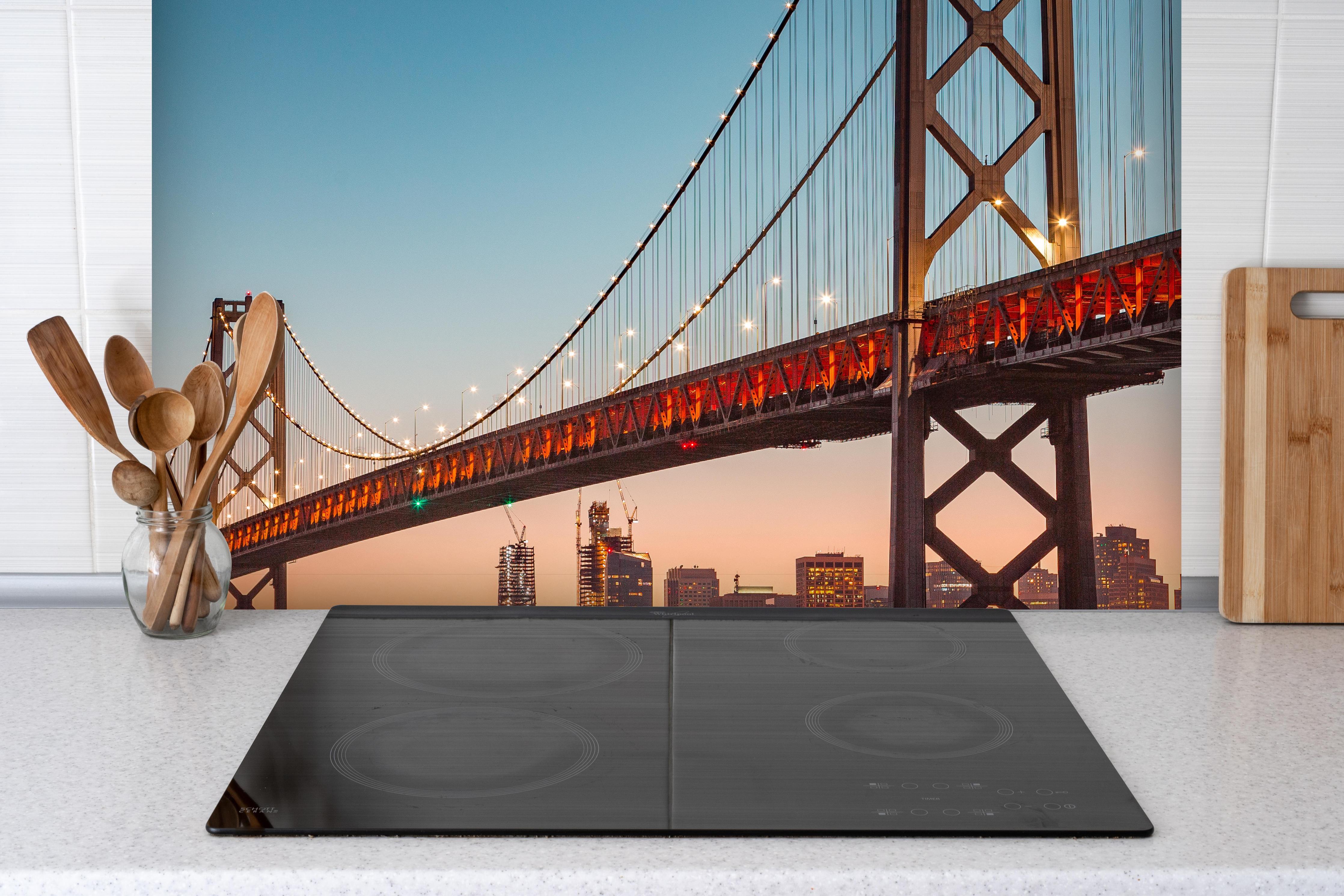 Spritzschutz - Oakland Bay Bridge bei Abendsonne hinter einem Cerankochfeld zwischen Holz-Kochutensilien