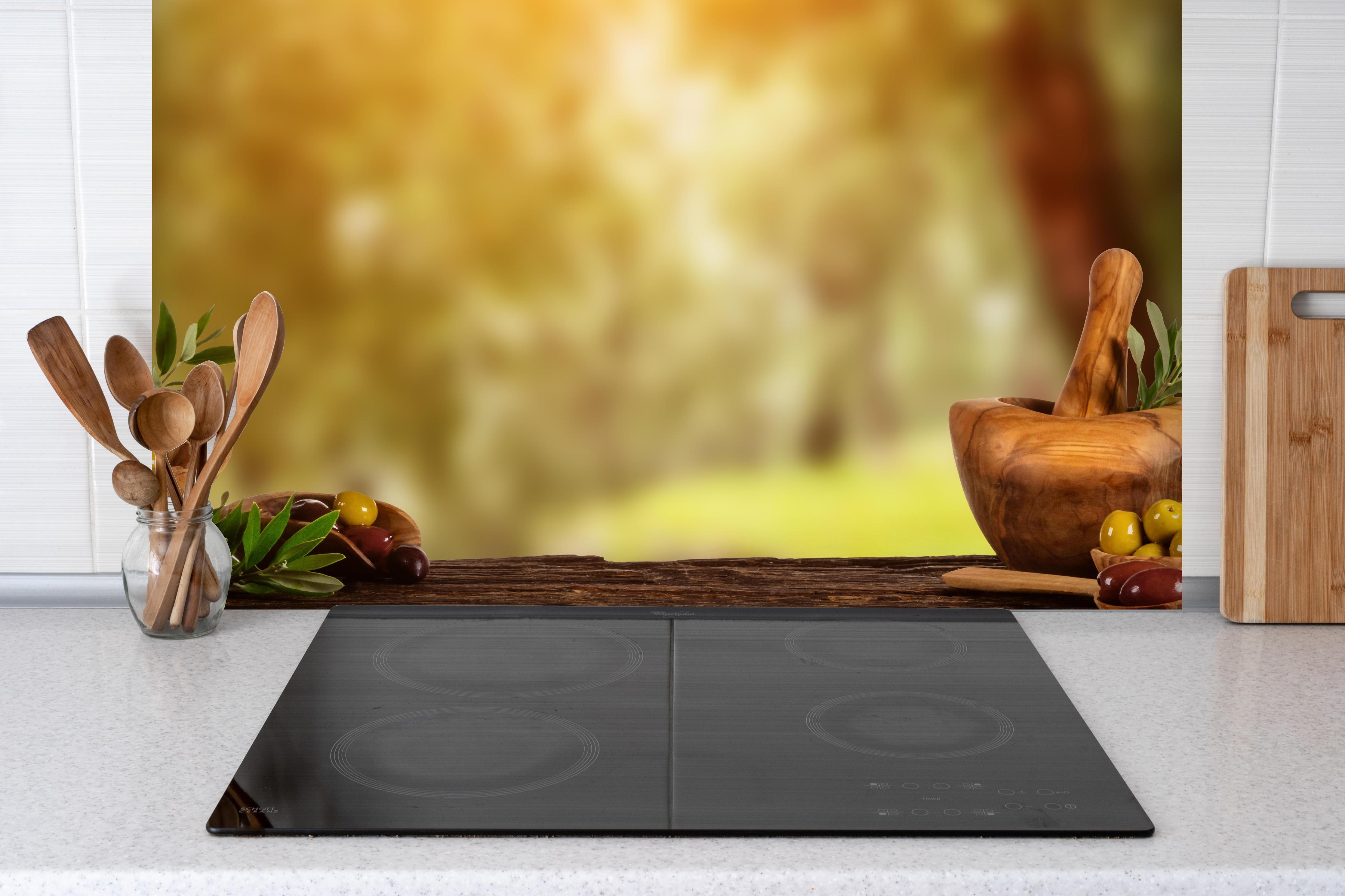 Spritzschutz - Olivenöl & Oliven hinter einem Cerankochfeld zwischen Holz-Kochutensilien