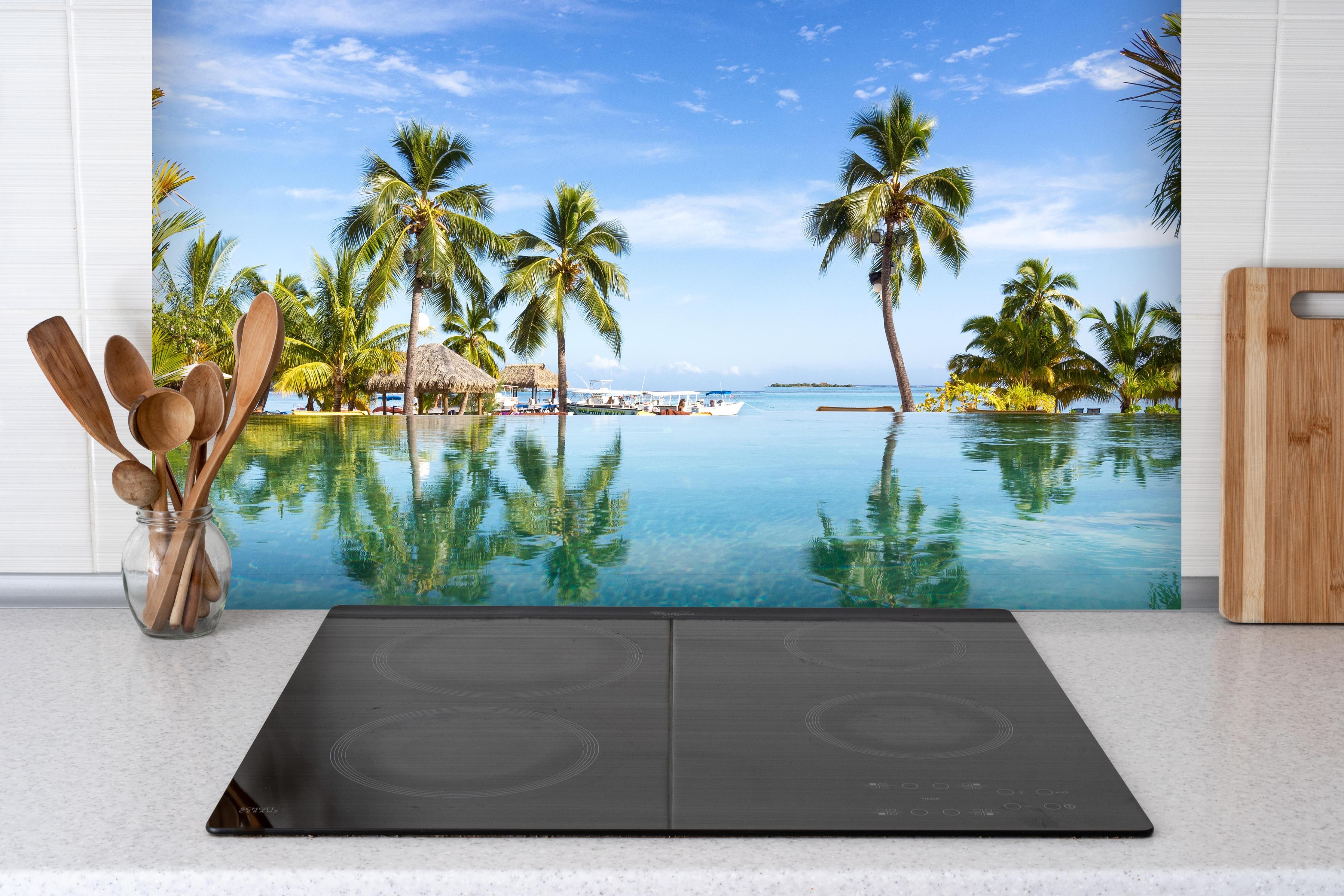 Spritzschutz - Panorama-Pool in der Karibik hinter einem Cerankochfeld zwischen Holz-Kochutensilien