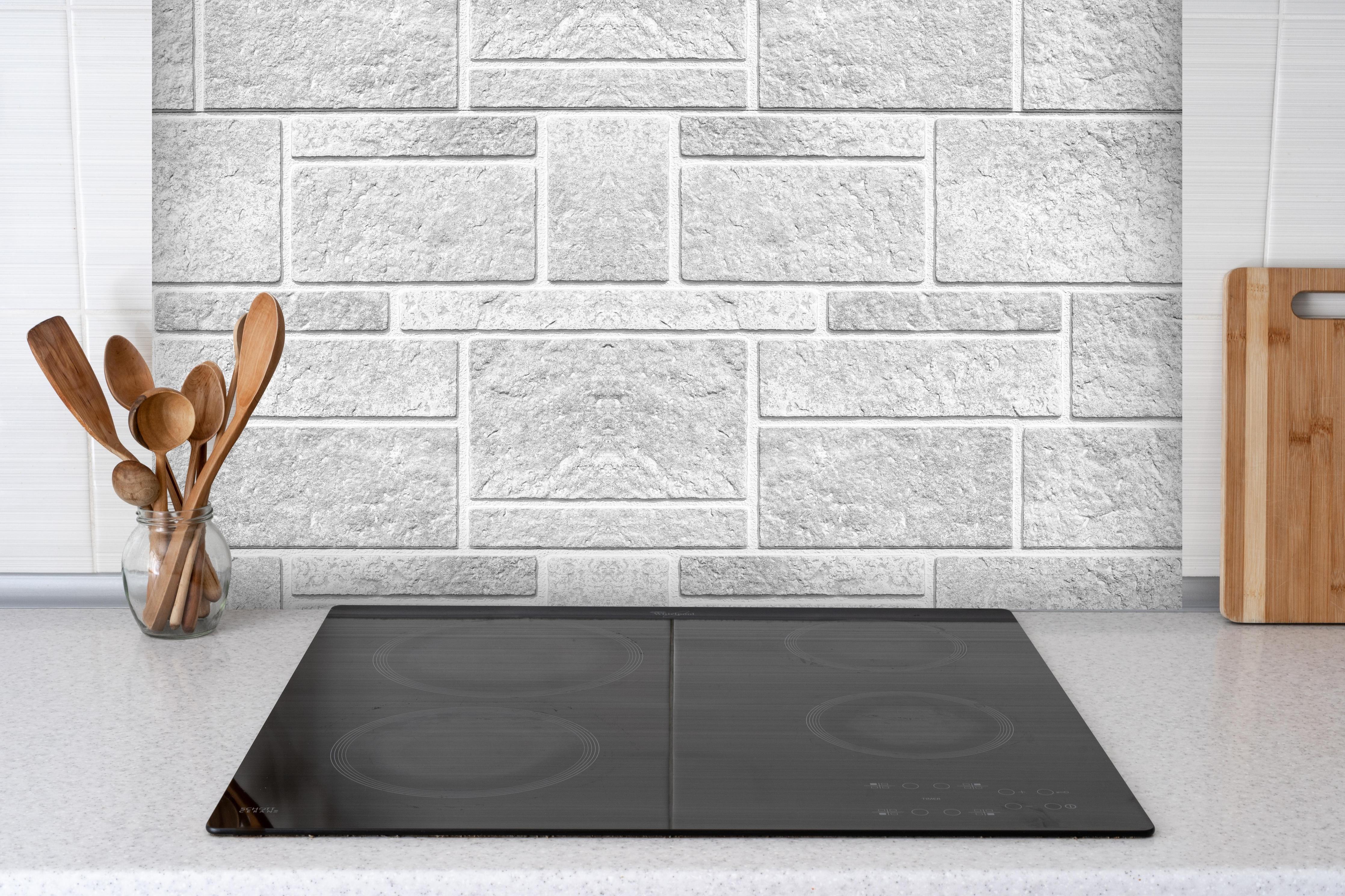 Spritzschutz - Panorama der rauen weißen Betonfliesen hinter einem Cerankochfeld zwischen Holz-Kochutensilien