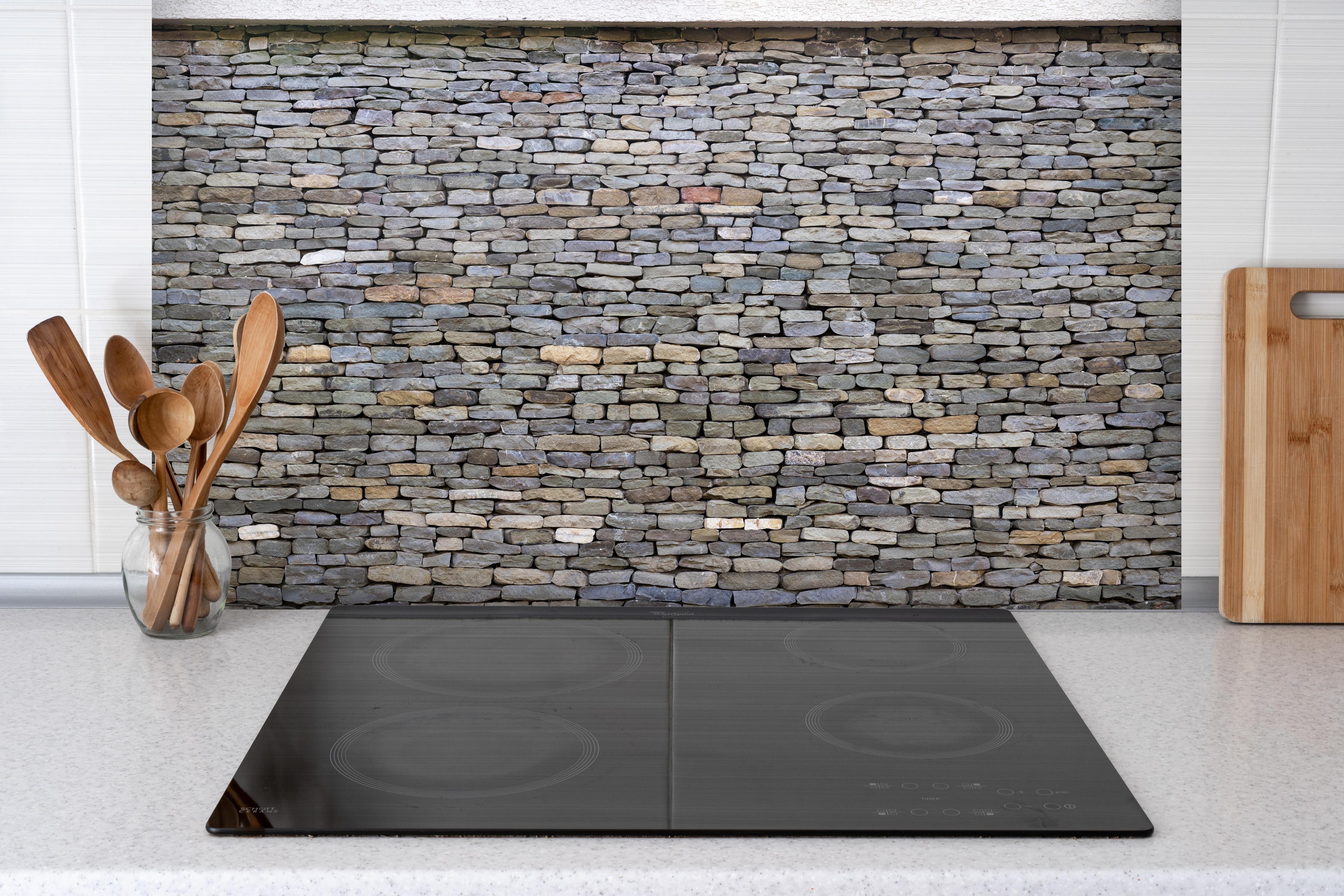 Spritzschutz - Pastellfarbene Steinmauer hinter einem Cerankochfeld zwischen Holz-Kochutensilien