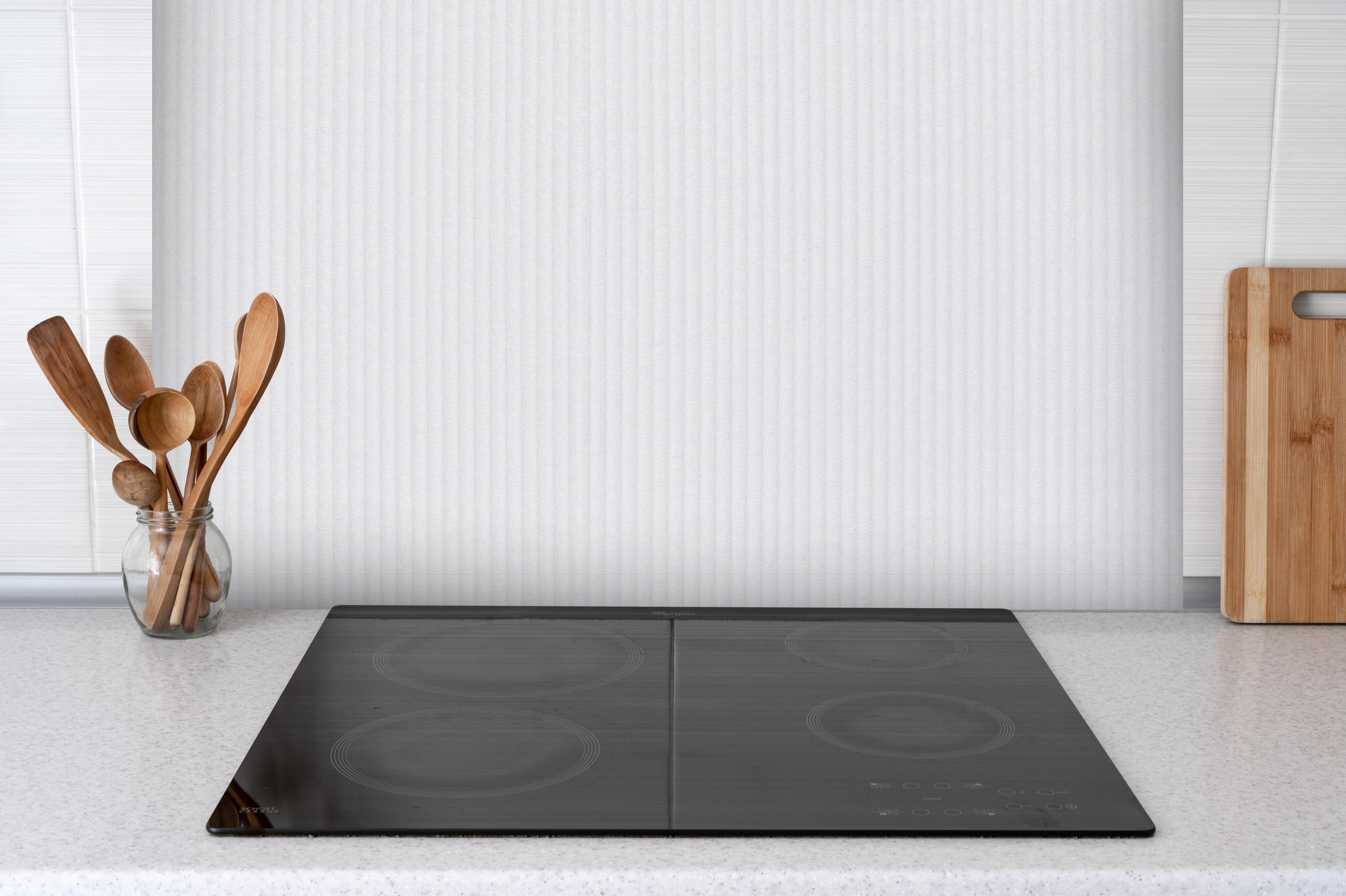 Spritzschutz - Pastellfarbiger lila Stoff hinter einem Cerankochfeld zwischen Holz-Kochutensilien