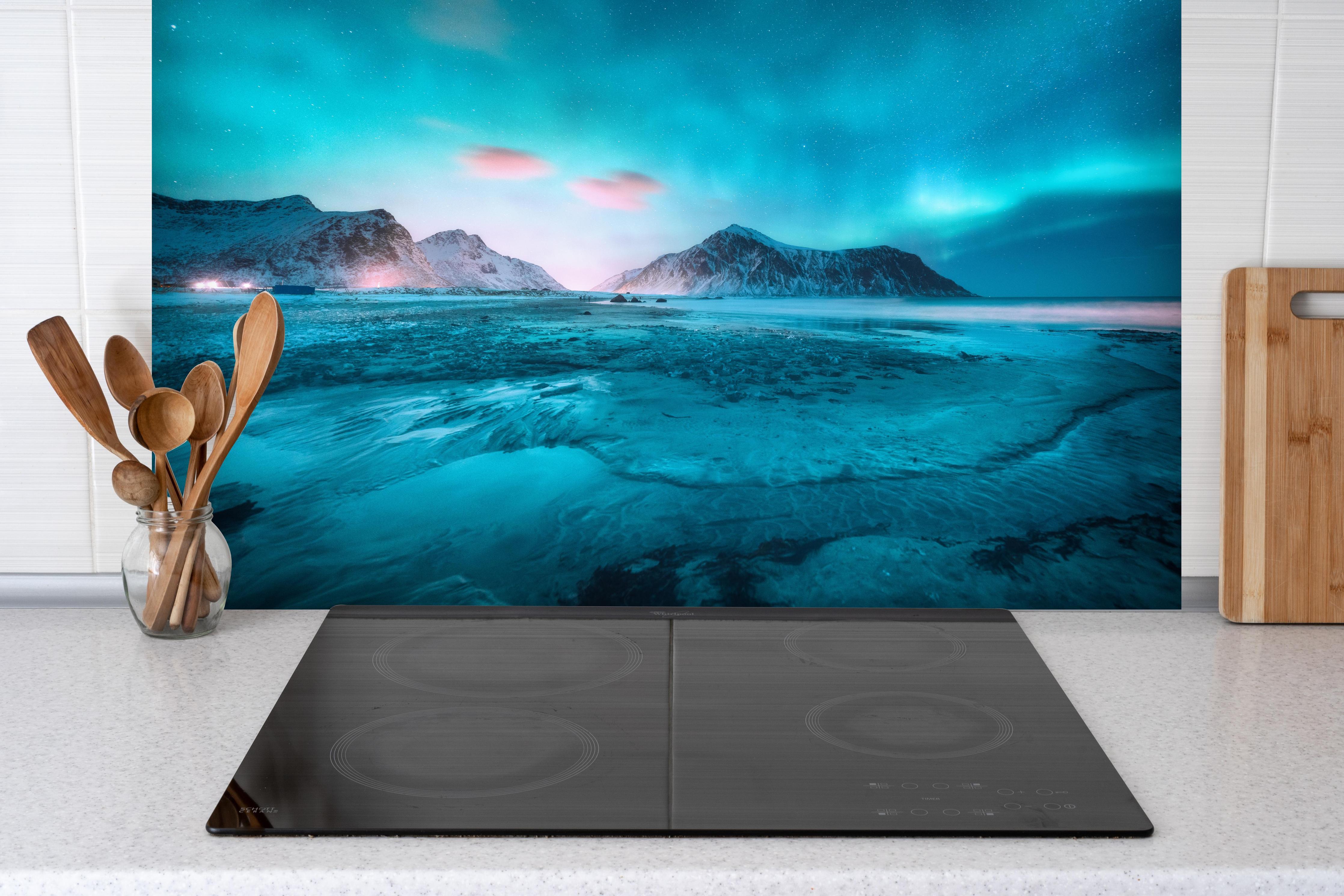 Spritzschutz - Polarlicht über schneebedeckten Berg mit Sandstrand hinter einem Cerankochfeld zwischen Holz-Kochutensilien