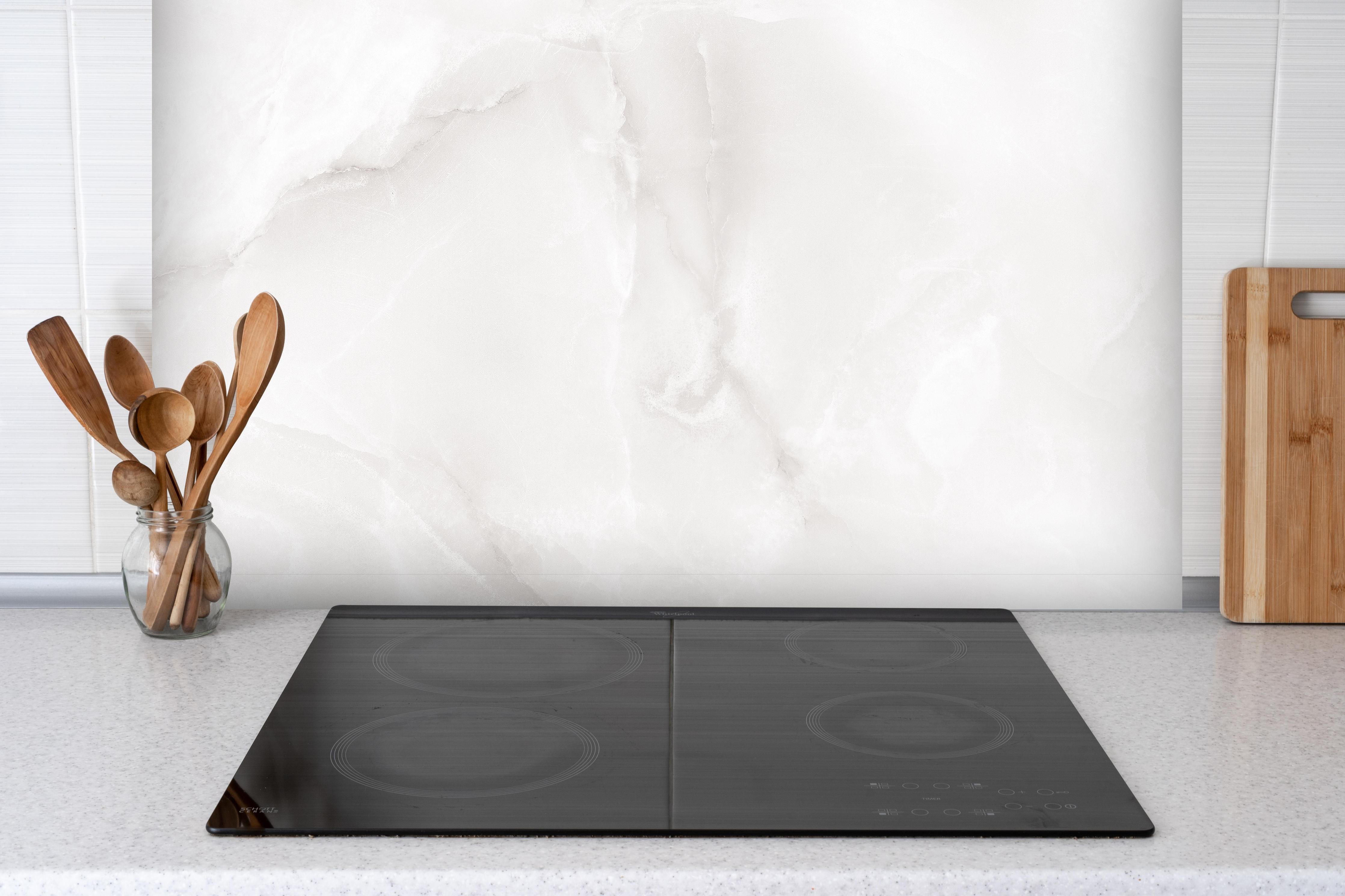 Spritzschutz - Polierter Onyxmarmor hinter einem Cerankochfeld zwischen Holz-Kochutensilien