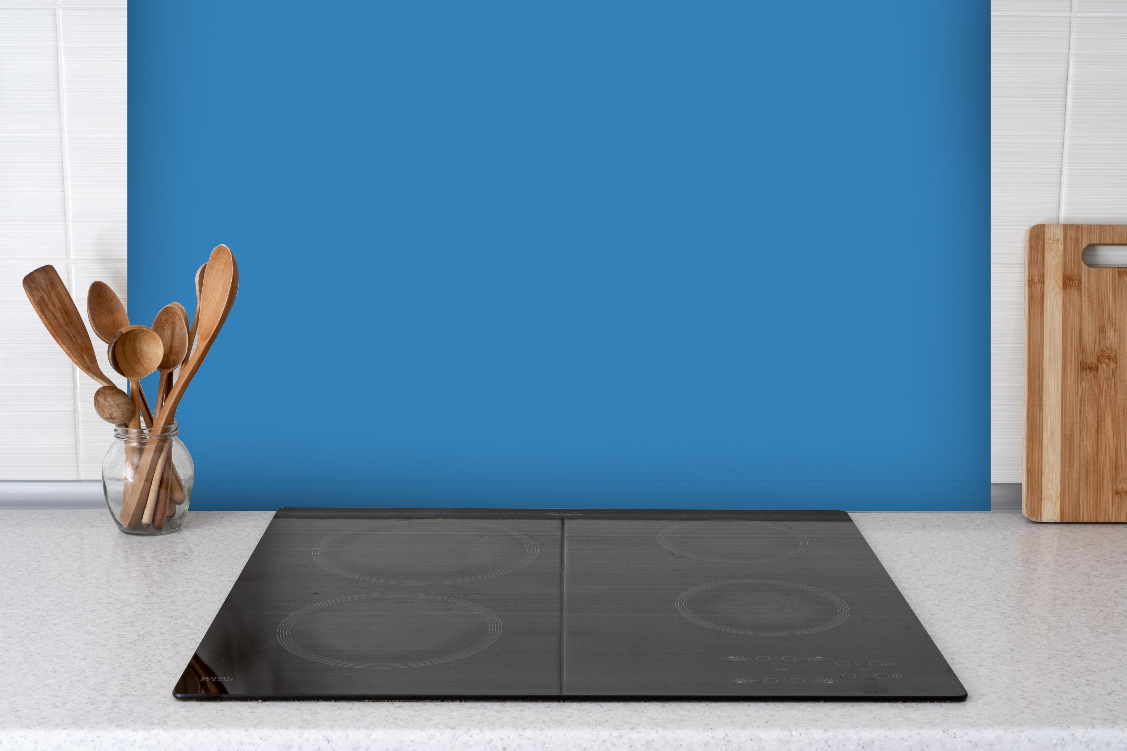 Spritzschutz - RAL 5012 (Hellblau) hinter einem Cerankochfeld zwischen Holz-Kochutensilien
