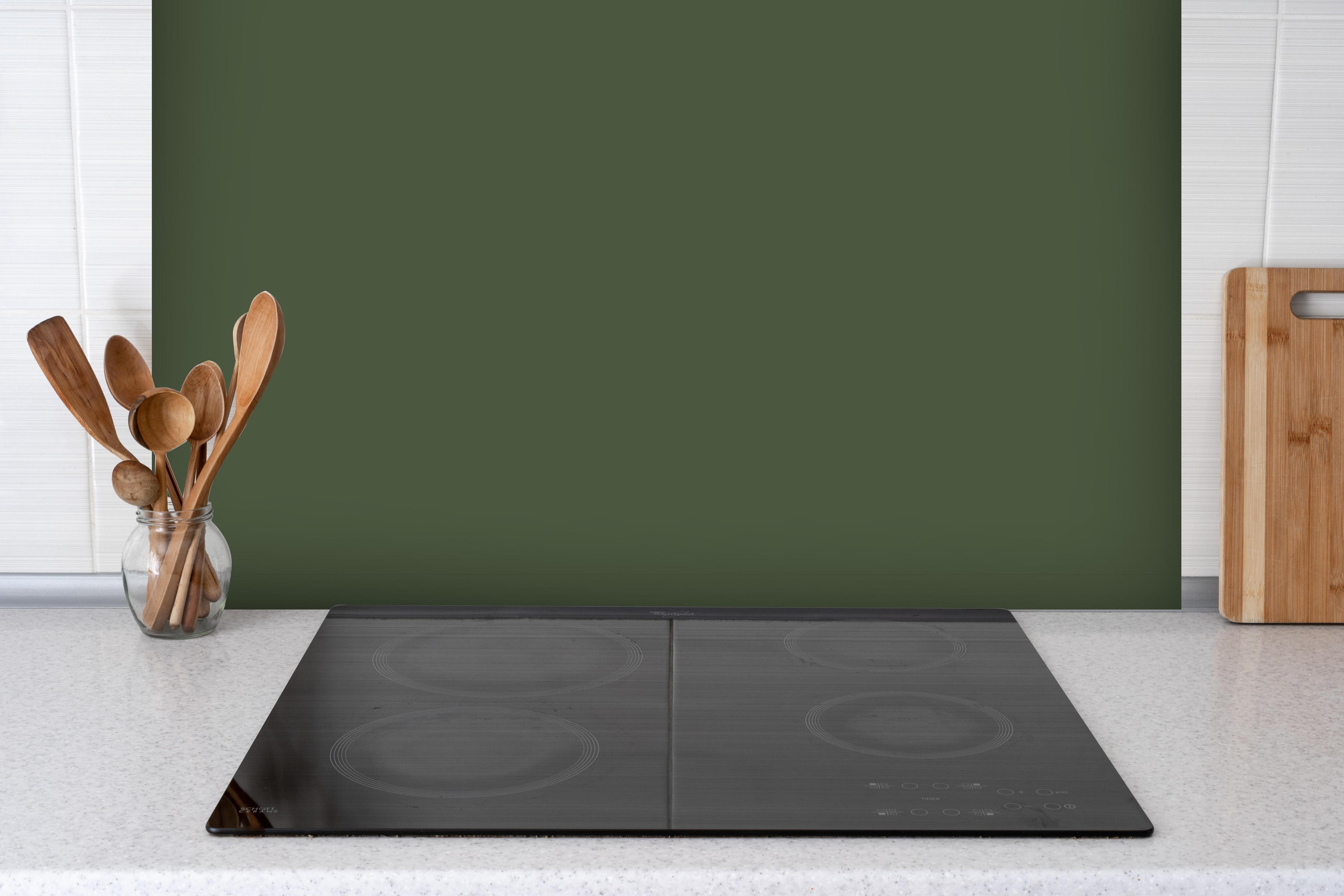Spritzschutz - RAL 6003 (olivgrün) hinter einem Cerankochfeld zwischen Holz-Kochutensilien