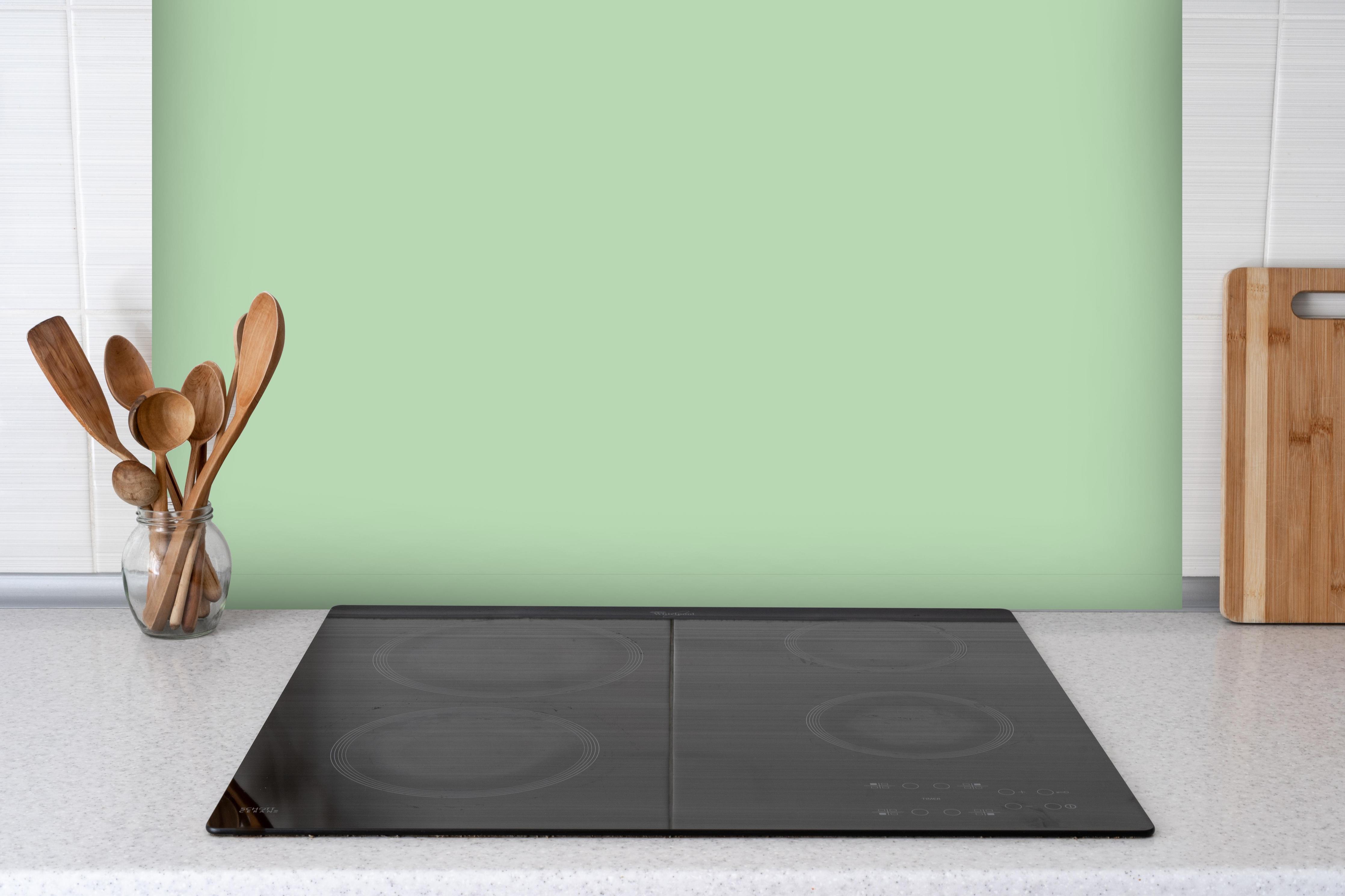 Spritzschutz - RAL 6019 (pastellgrün) hinter einem Cerankochfeld zwischen Holz-Kochutensilien