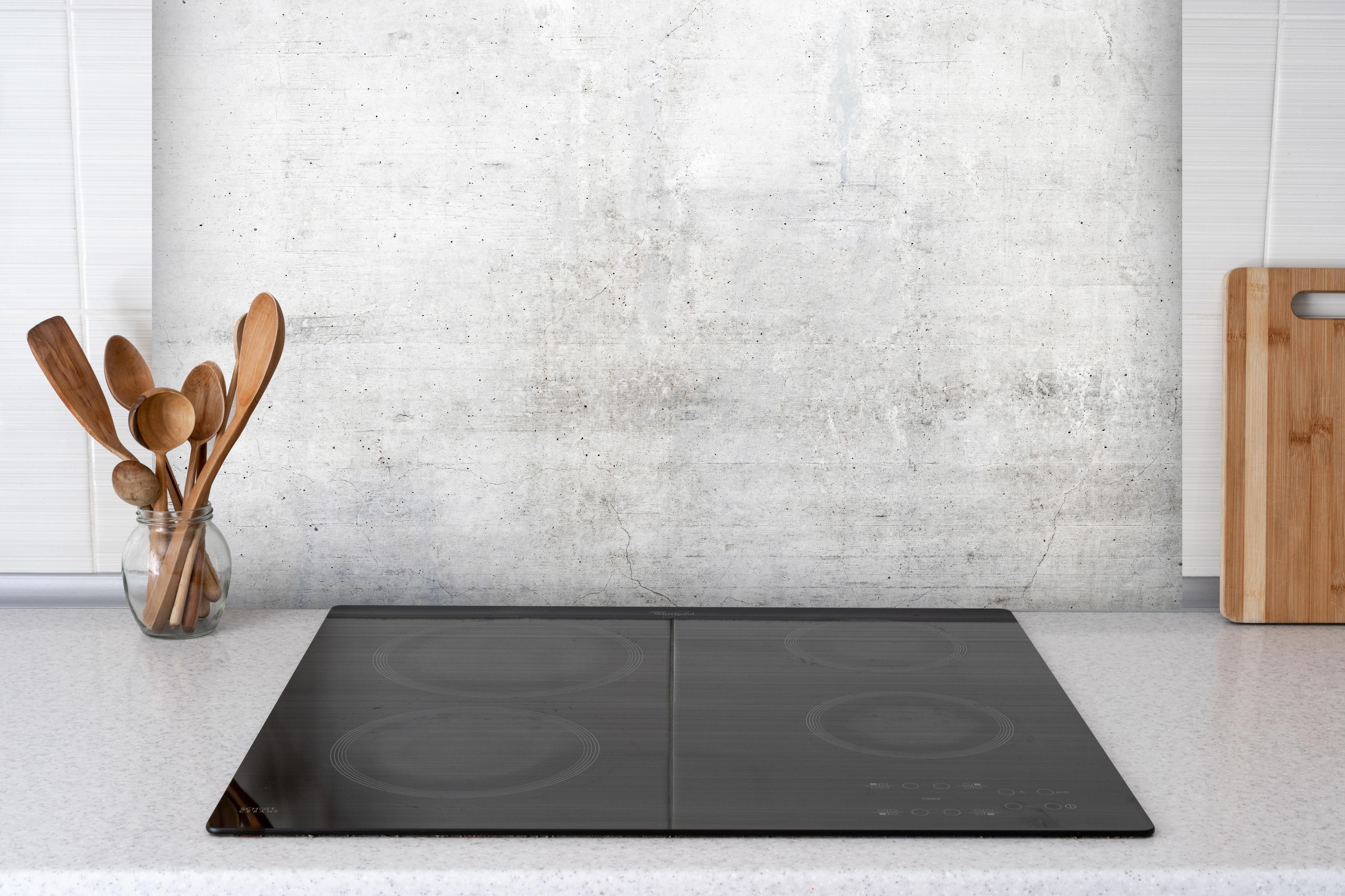 Spritzschutz - Rauer weißer Beton hinter einem Cerankochfeld zwischen Holz-Kochutensilien
