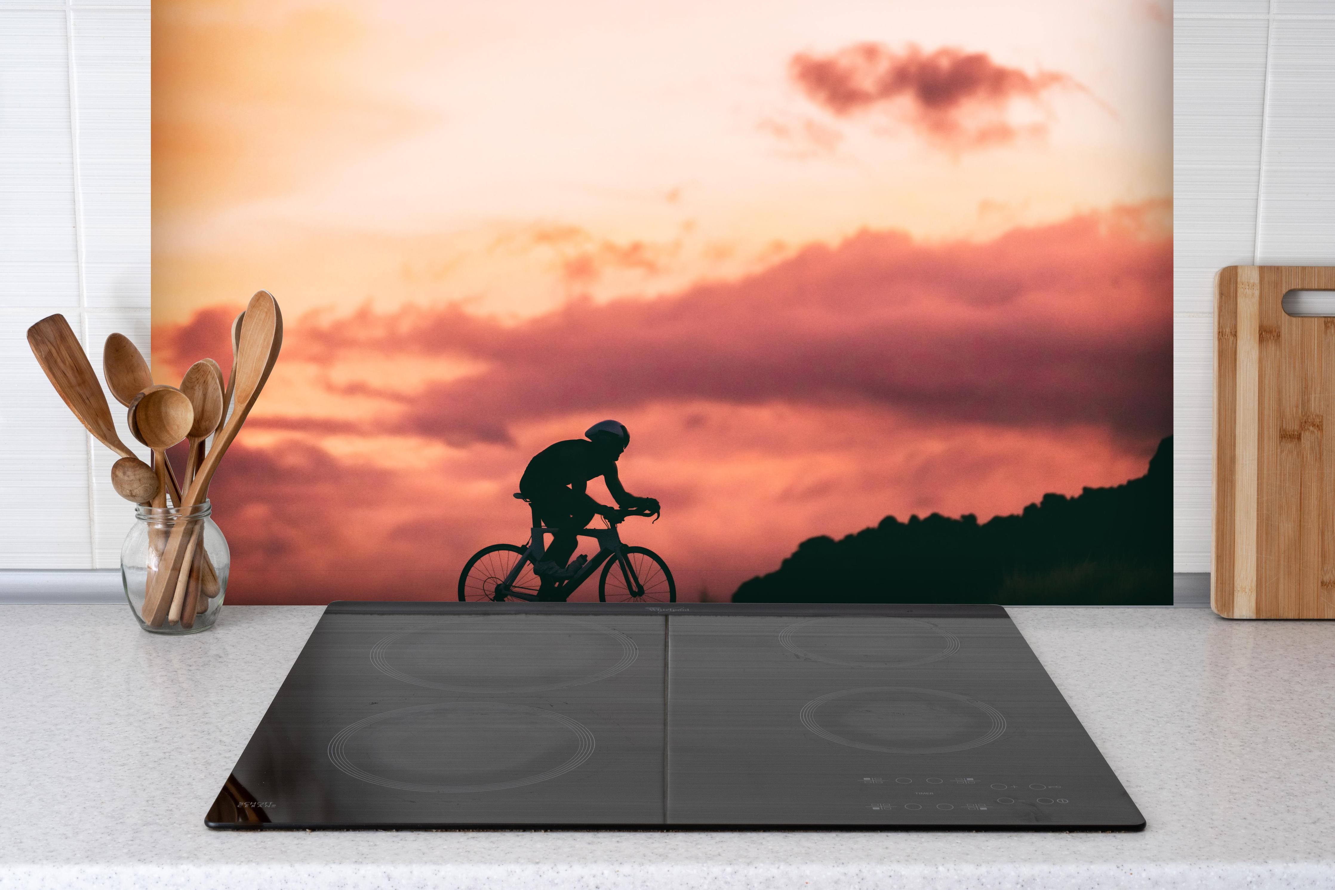 Spritzschutz - Rennradfahrer hinter einem Cerankochfeld zwischen Holz-Kochutensilien