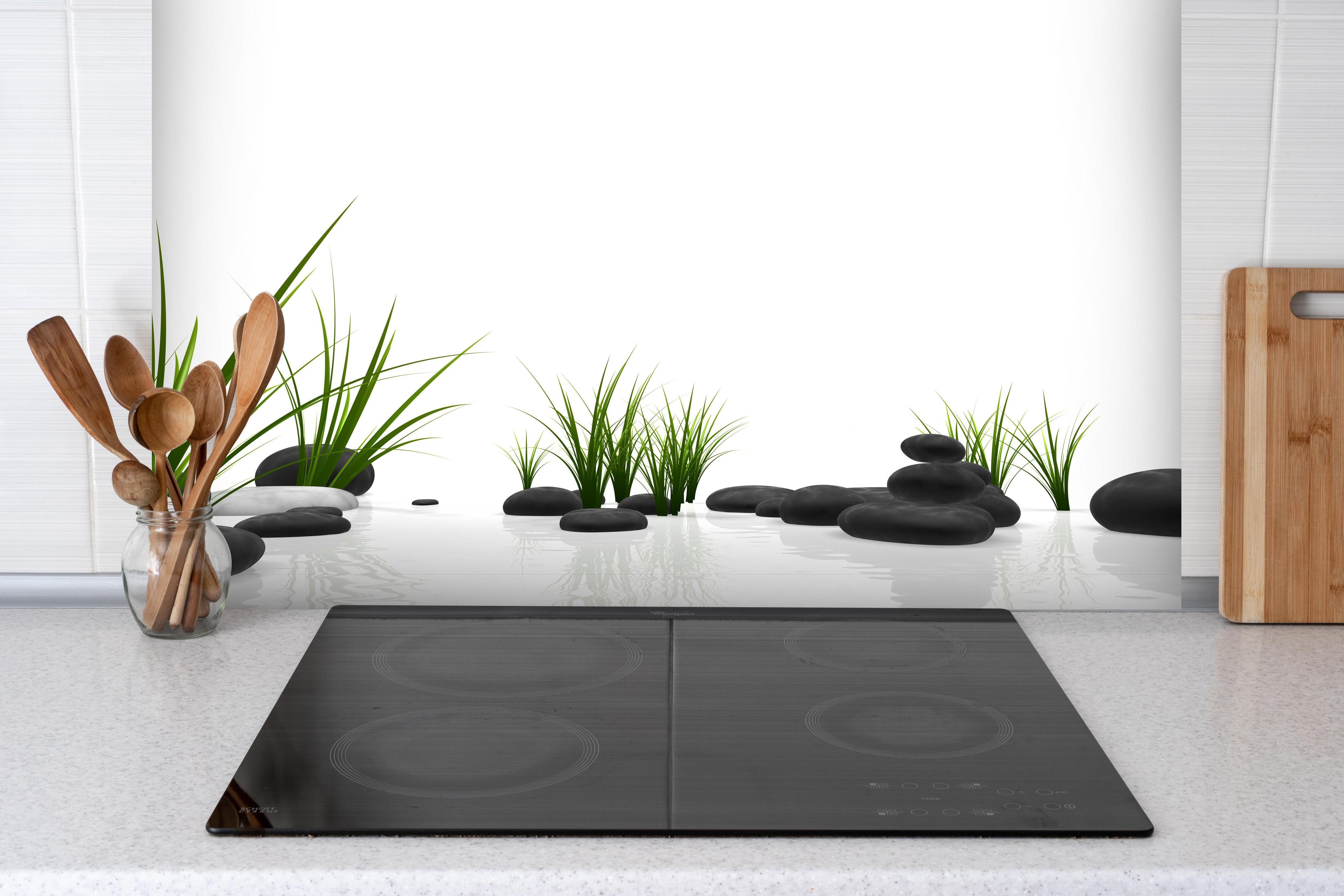 Spritzschutz - Ruhiges Steine Gefilde mit Gras und Wasser hinter einem Cerankochfeld zwischen Holz-Kochutensilien