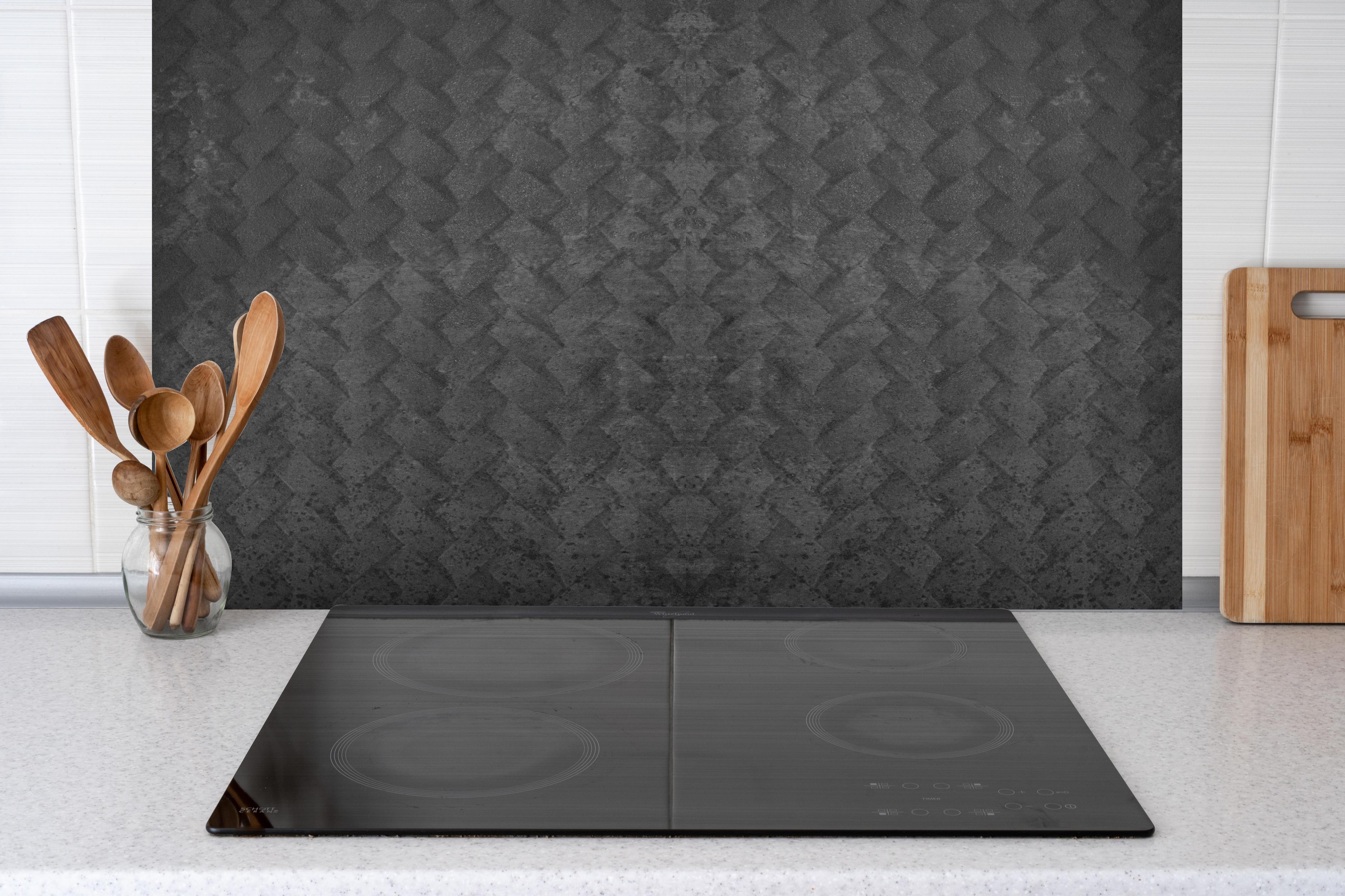Spritzschutz - Schwarze geometrisches Betonwand hinter einem Cerankochfeld zwischen Holz-Kochutensilien