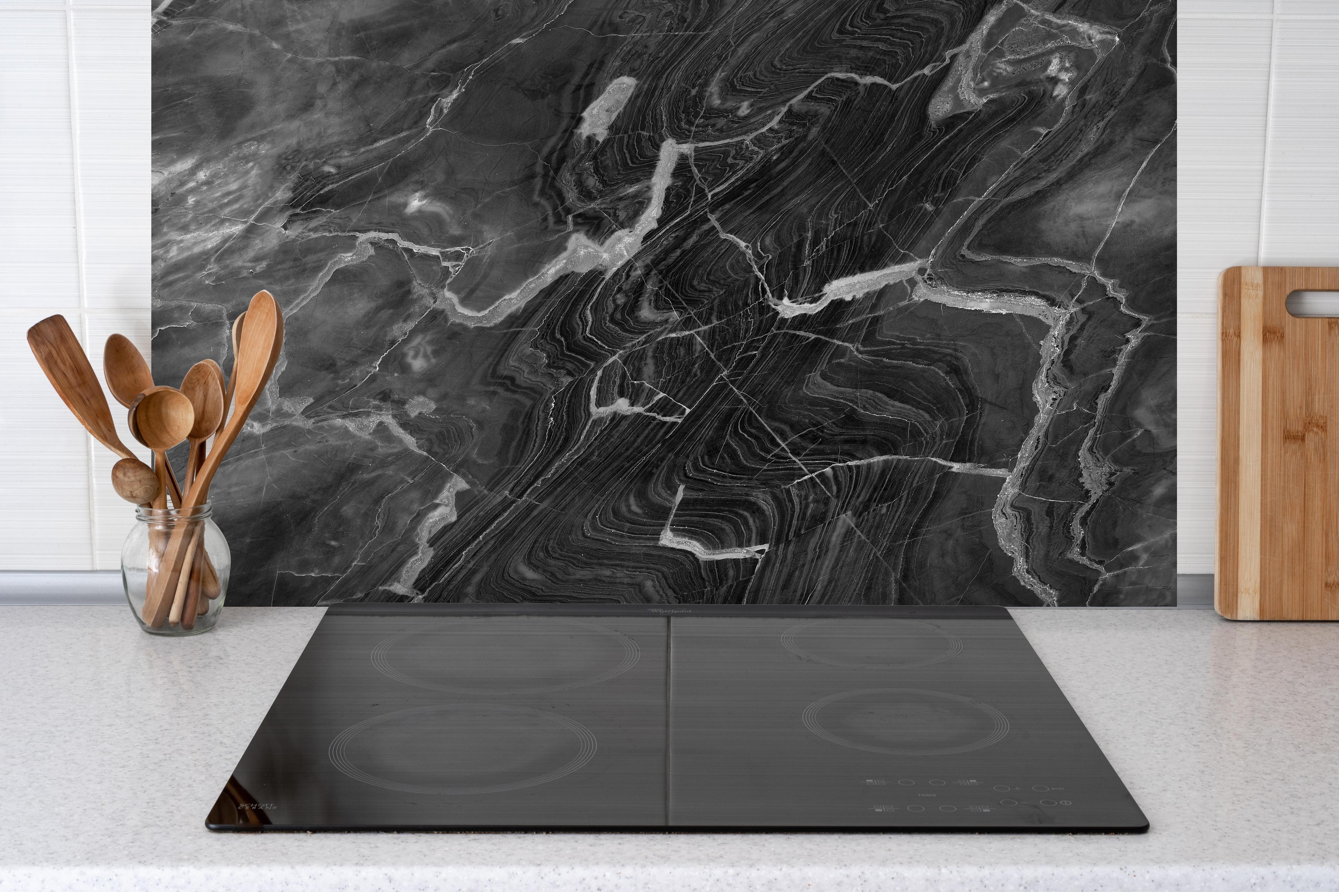 Spritzschutz - Schwarzer Marmor mit weißen Adern hinter einem Cerankochfeld zwischen Holz-Kochutensilien