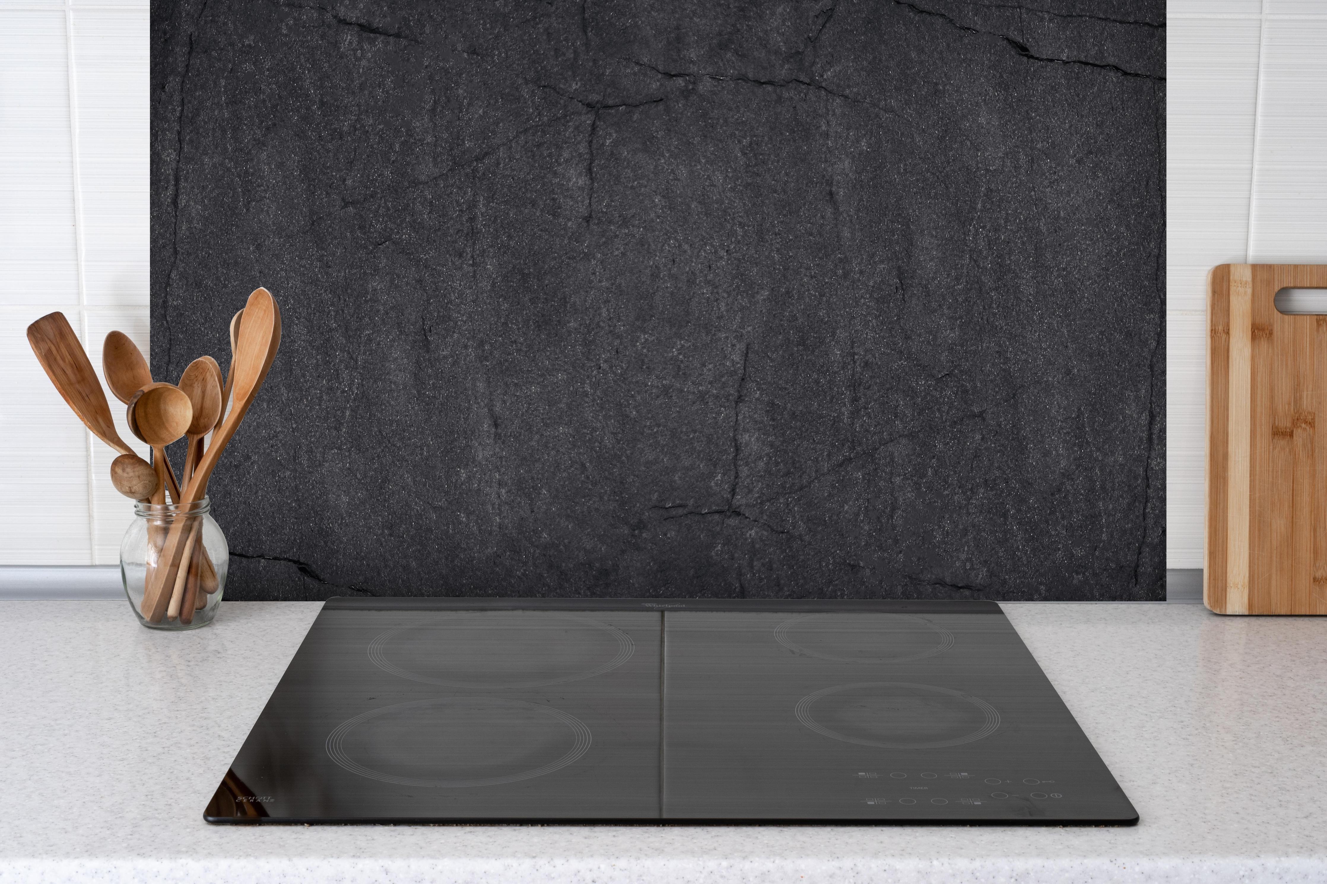 Spritzschutz - Schwarzes Felsgestein hinter einem Cerankochfeld zwischen Holz-Kochutensilien