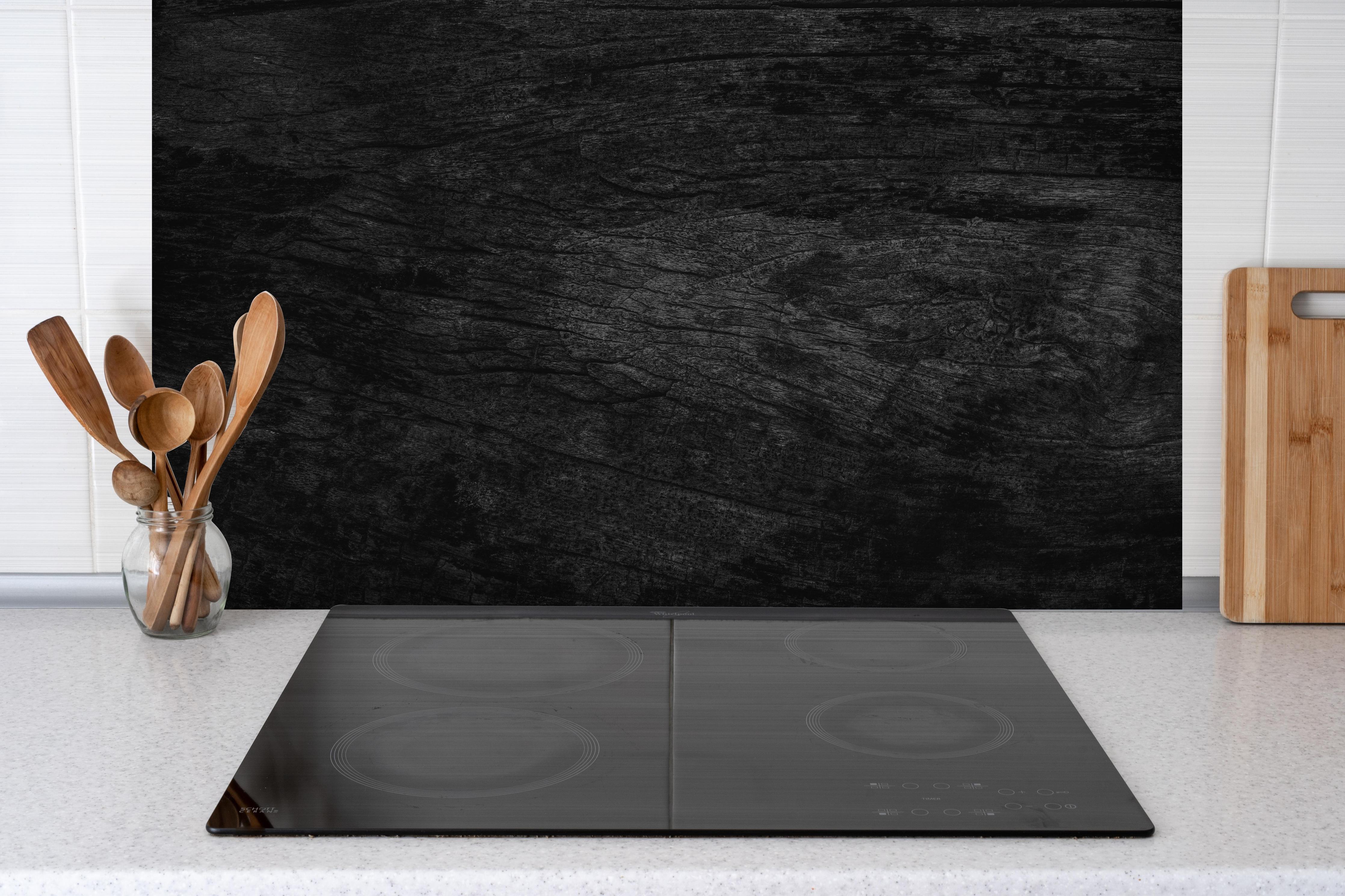 Spritzschutz - Schwarzes Holz Muster mit Textur hinter einem Cerankochfeld zwischen Holz-Kochutensilien