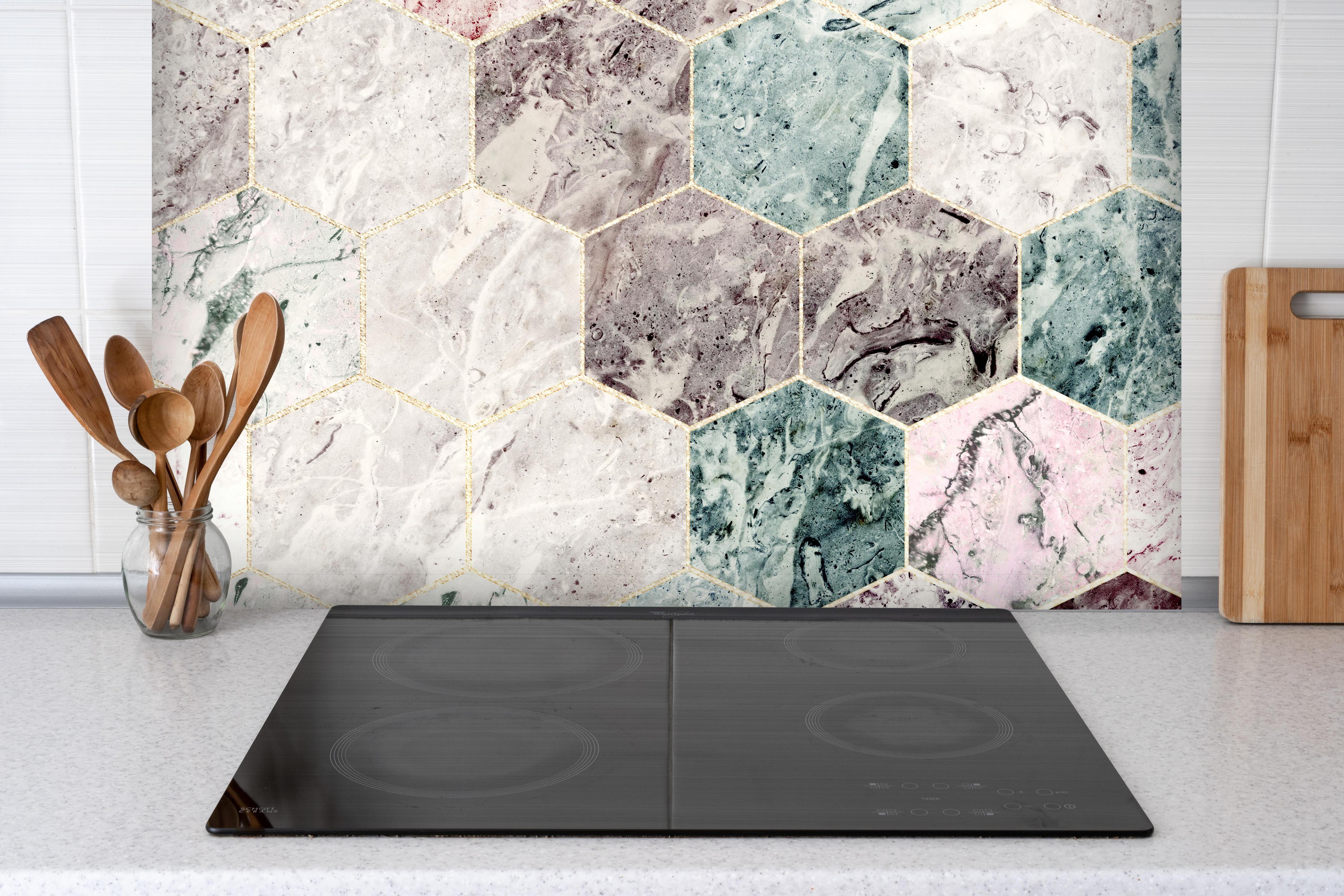 Spritzschutz - Sechseckiger dunkler Marmor mit Goldumrandung hinter einem Cerankochfeld zwischen Holz-Kochutensilien