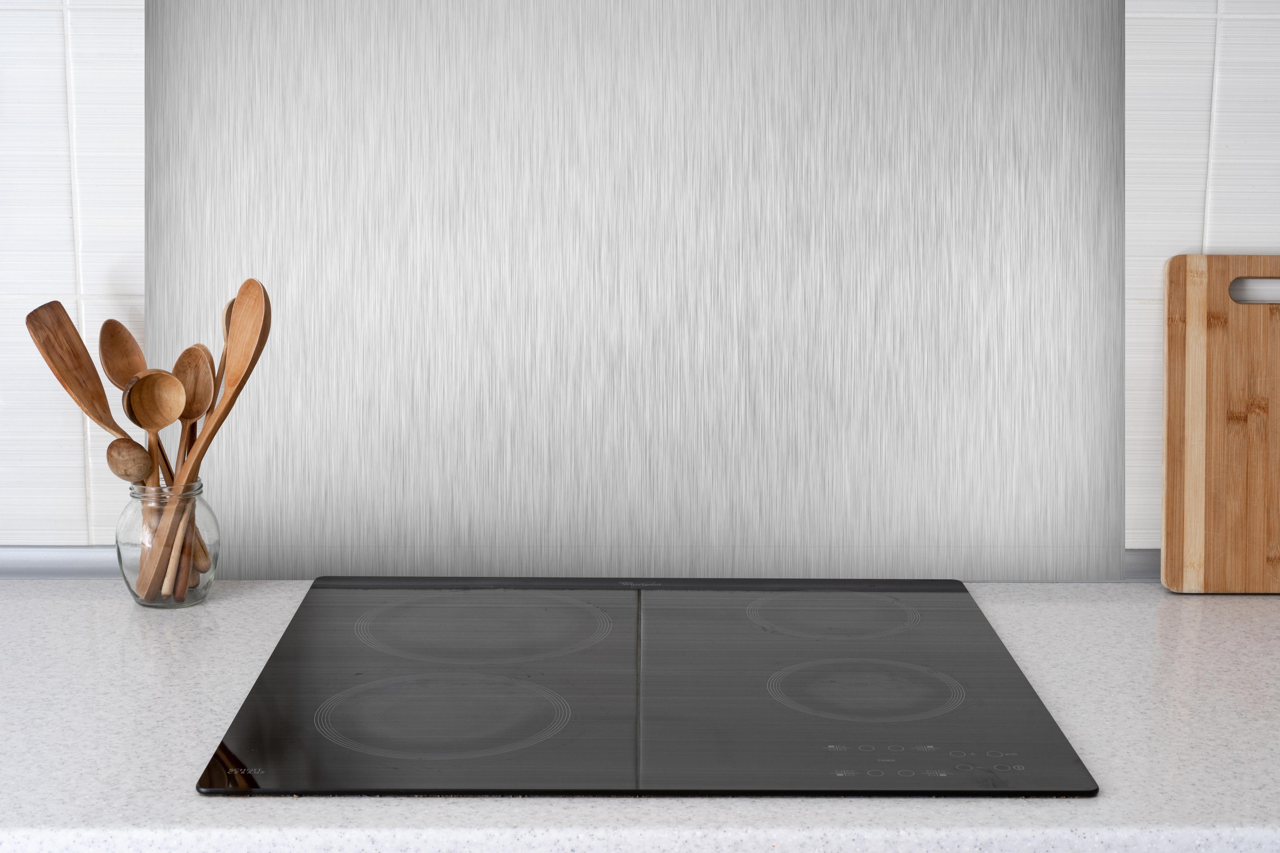 Spritzschutz - Silberne belichtete Oberfläche hinter einem Cerankochfeld zwischen Holz-Kochutensilien