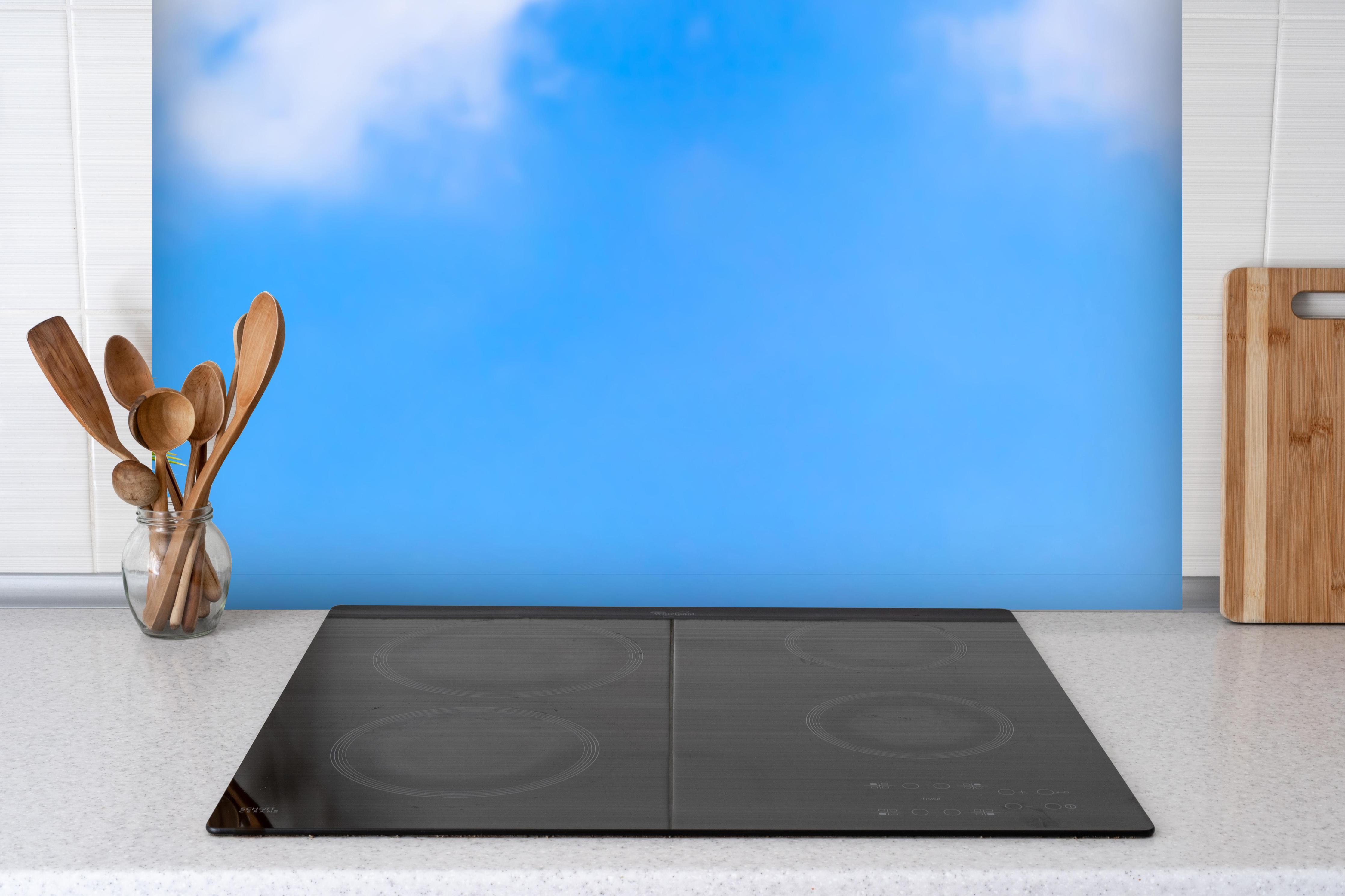 Spritzschutz - Sonne strahlt auf Palme hinter einem Cerankochfeld zwischen Holz-Kochutensilien