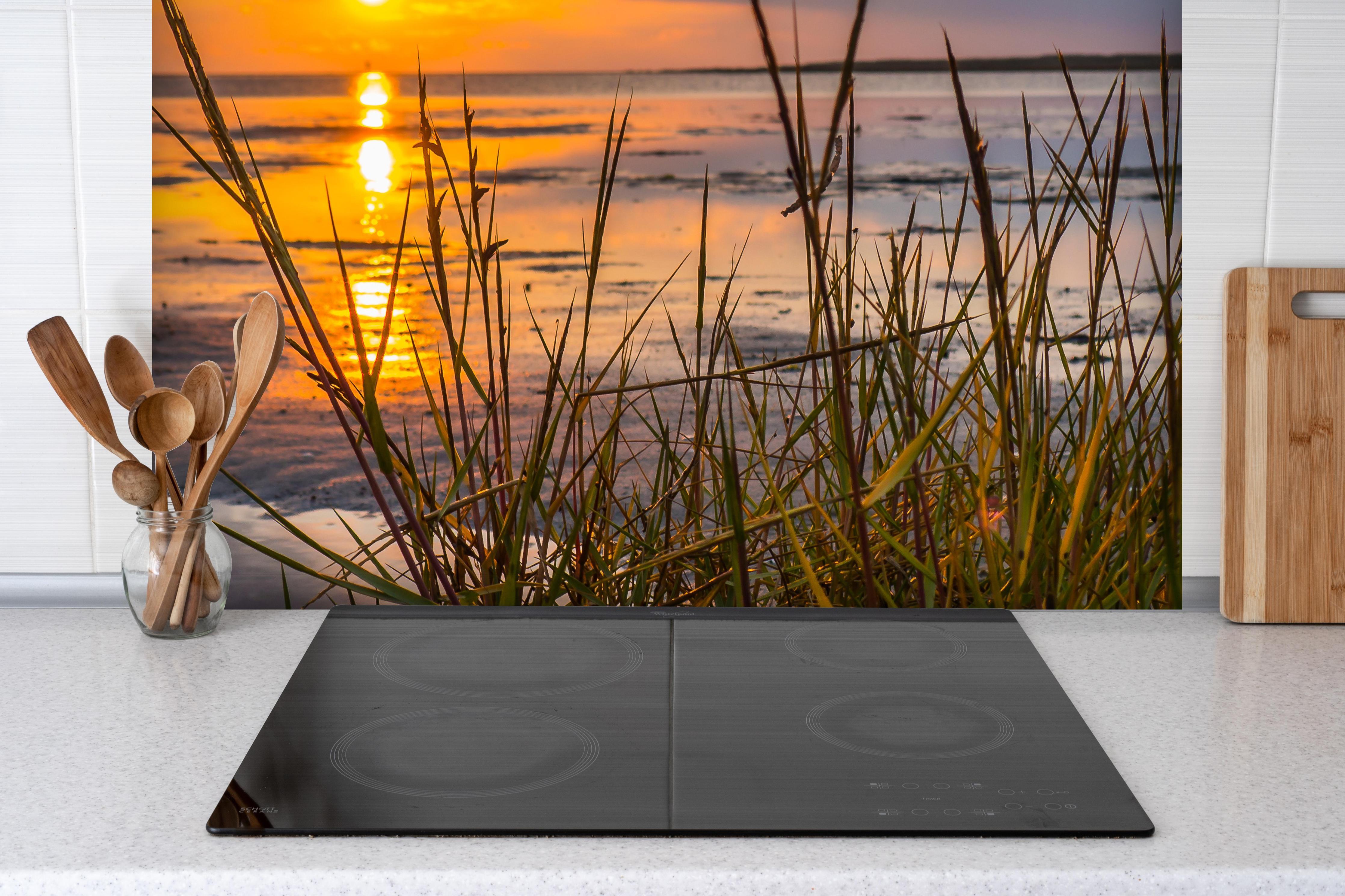 Spritzschutz - Sonnenuntergang im Wattenmeer an der Nordsee hinter einem Cerankochfeld zwischen Holz-Kochutensilien