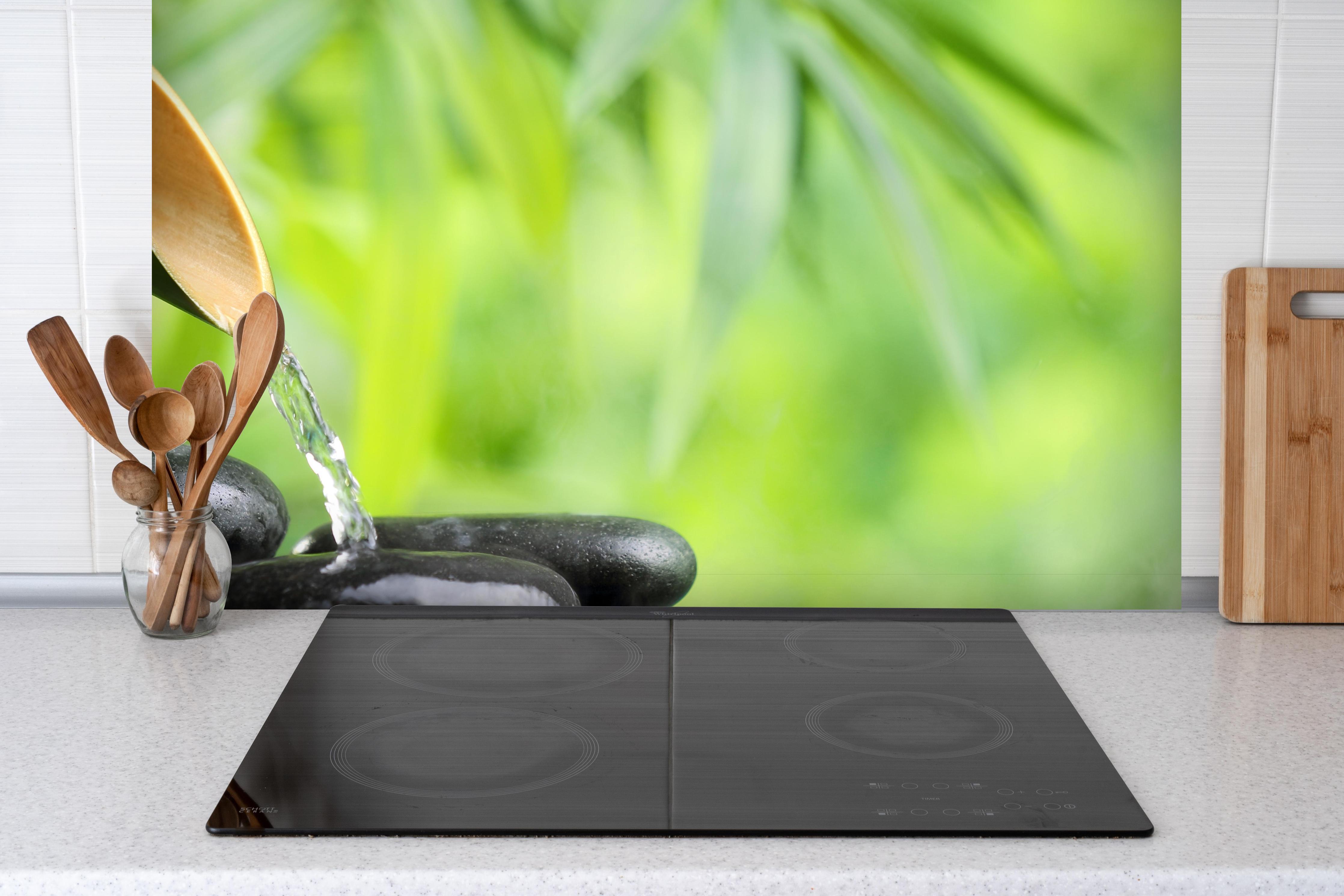 Spritzschutz - Spa-Stillleben mit Bambusbrunnen hinter einem Cerankochfeld zwischen Holz-Kochutensilien